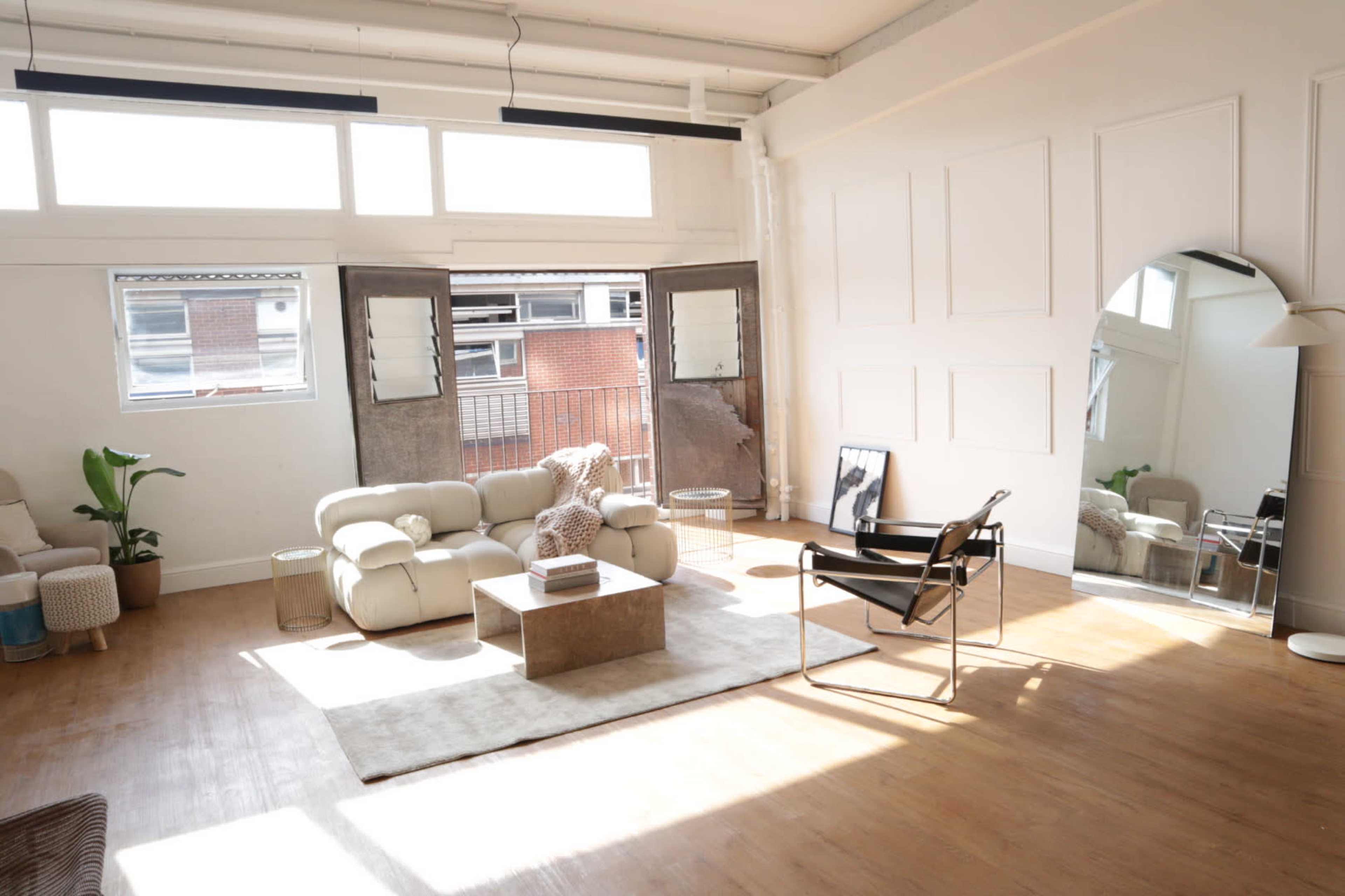 A bright, spacious living area features modern furniture, large windows, and wooden flooring.