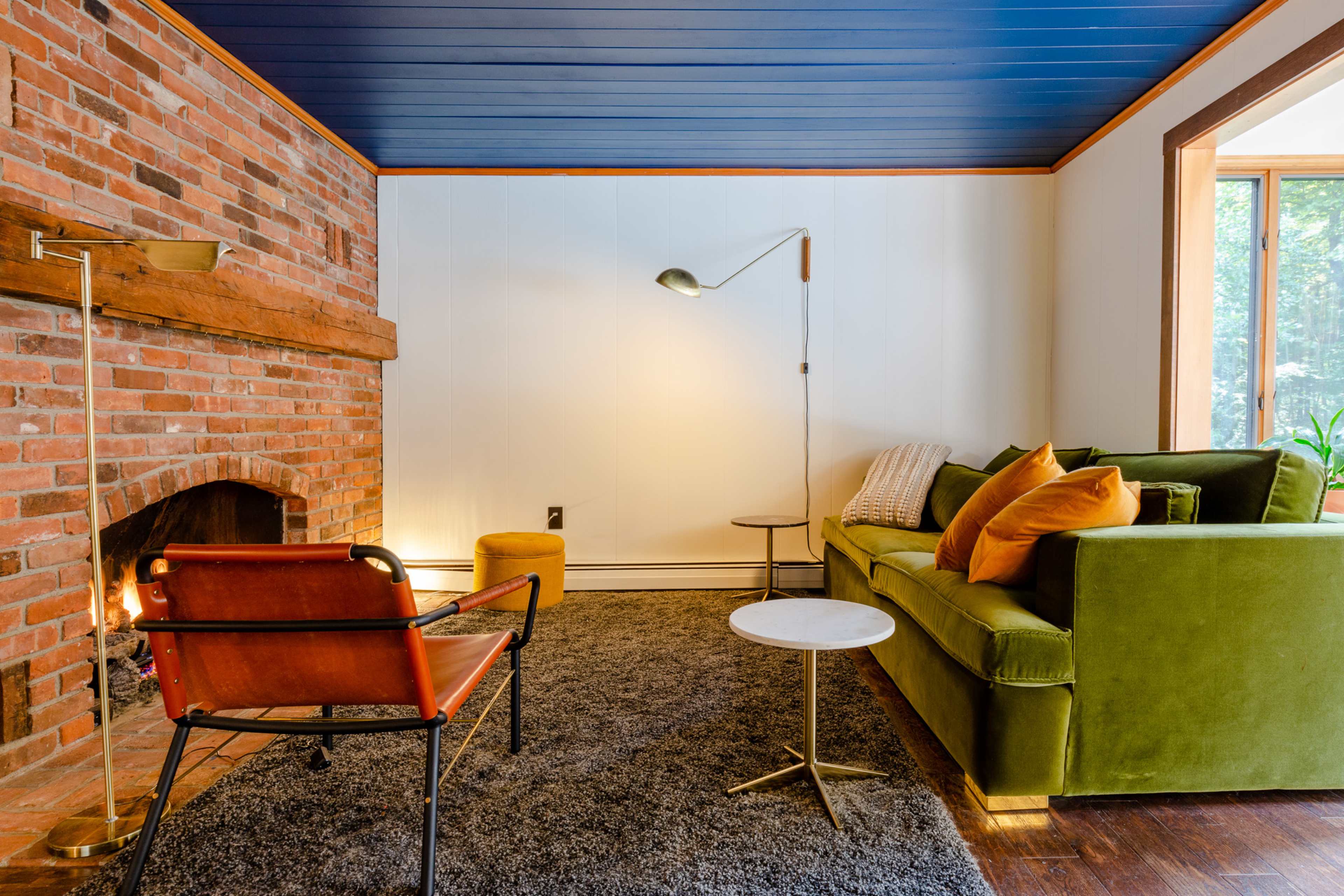 A cozy living room features a brick fireplace, a green sofa with decorative pillows, a wooden side table, and a stylish floor lamp.