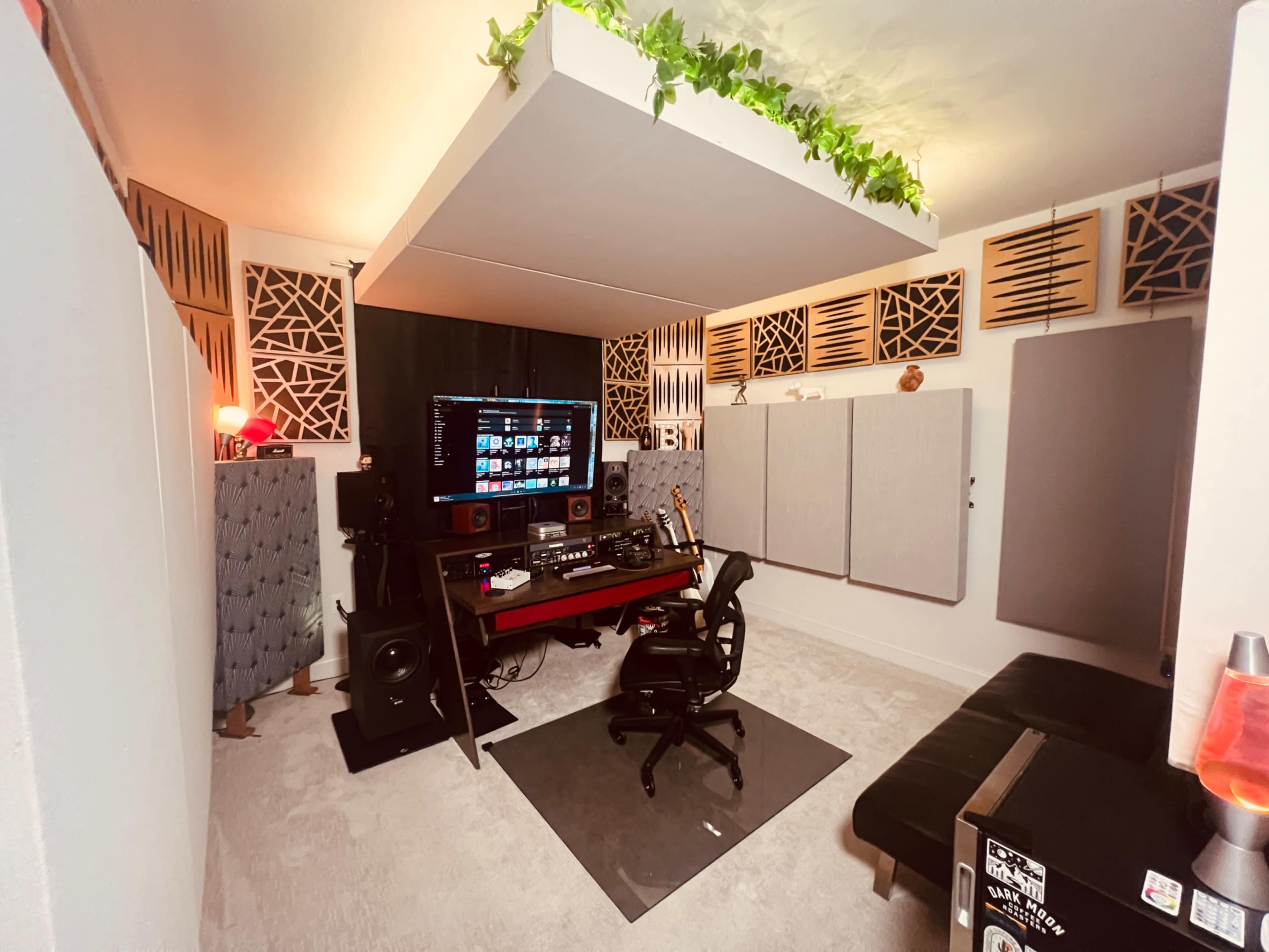 The image shows a music production studio featuring soundproofing panels, a desk with audio equipment, and decorative elements like plants.