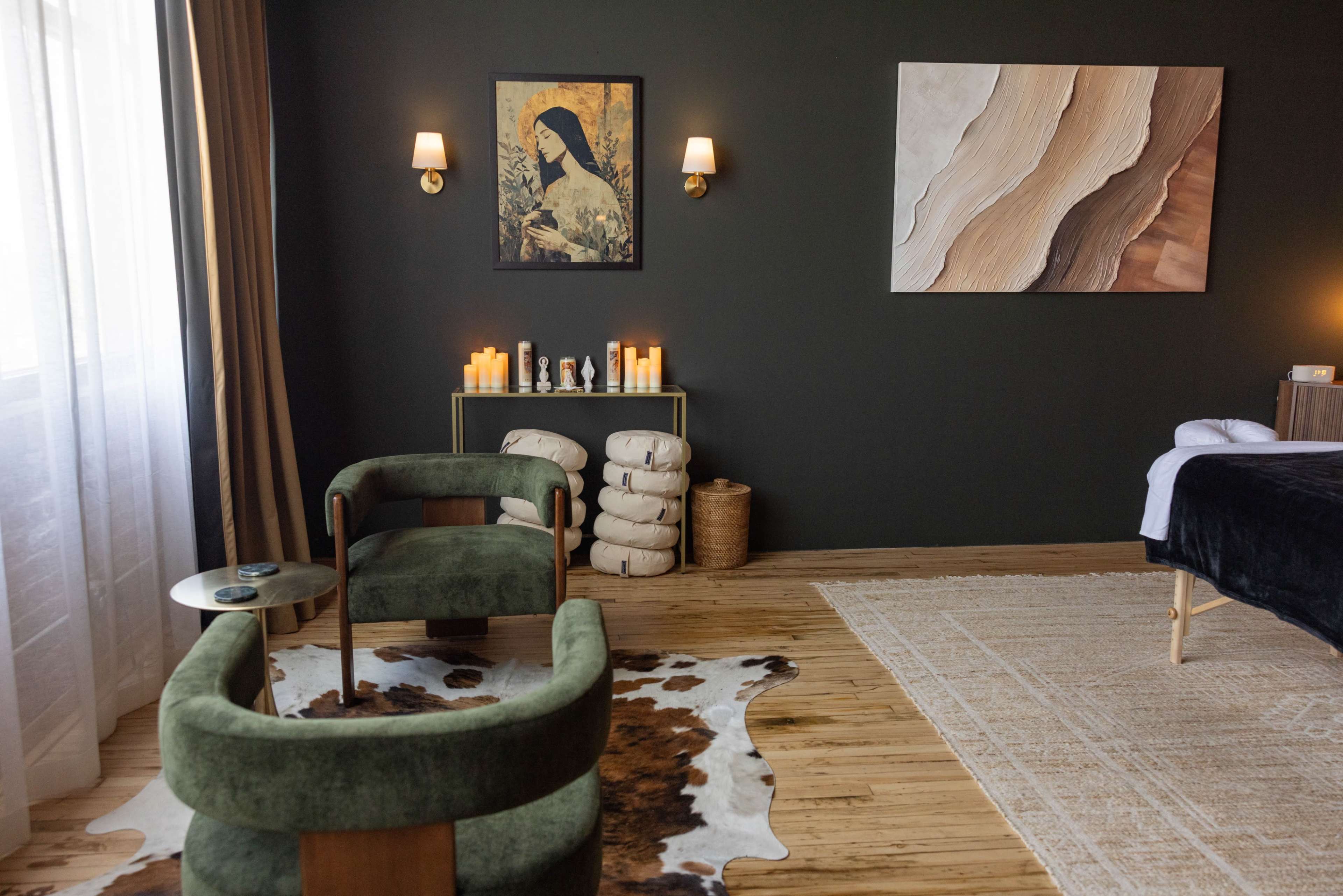 The image shows a modern interior room featuring two green armchairs, a wooden floor, wall art, and decorative elements including candles and a fur rug.