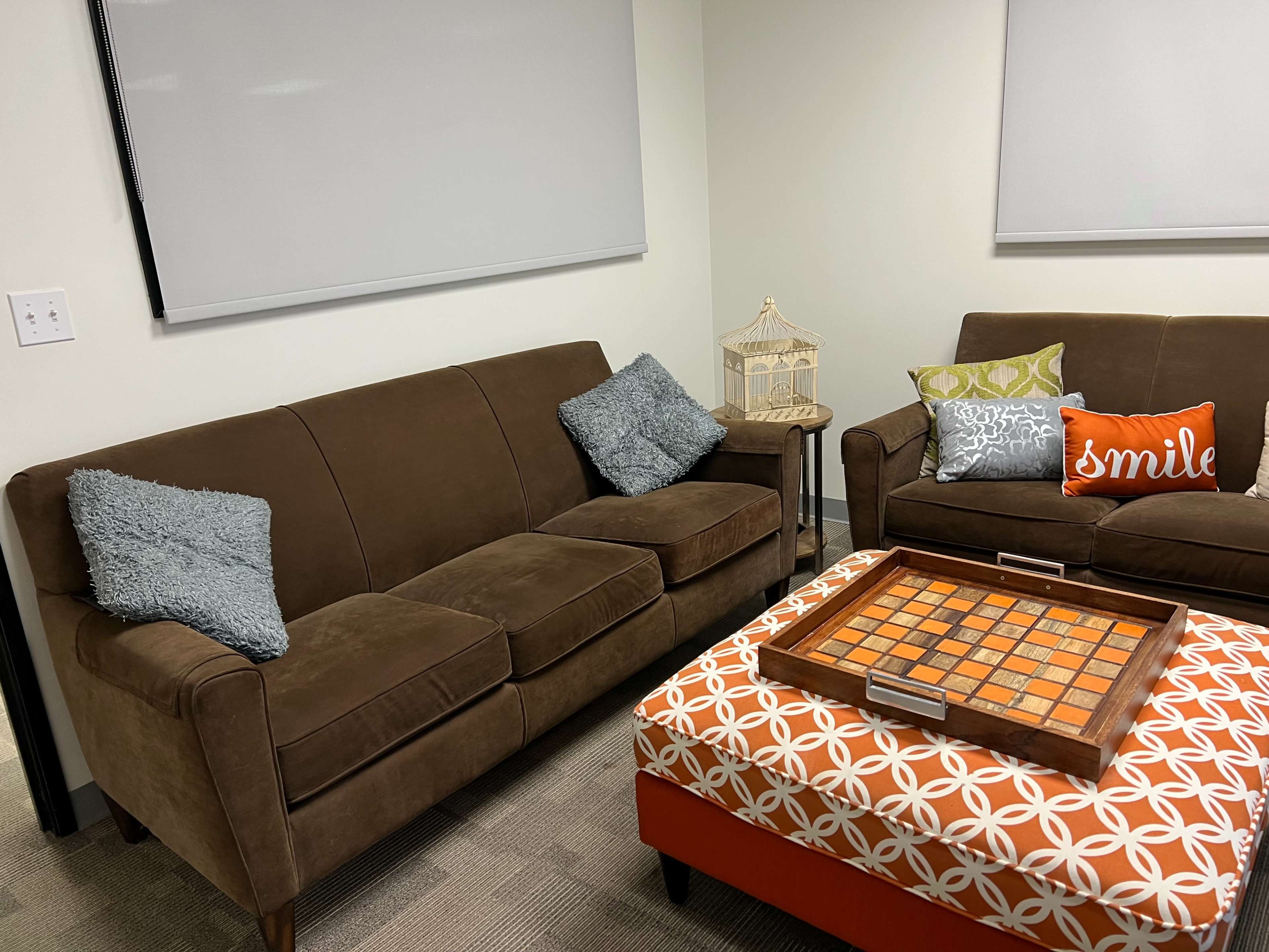 A cozy seating area with a brown sofa, a matching chair, and an orange and white patterned coffee table with a game board on it.