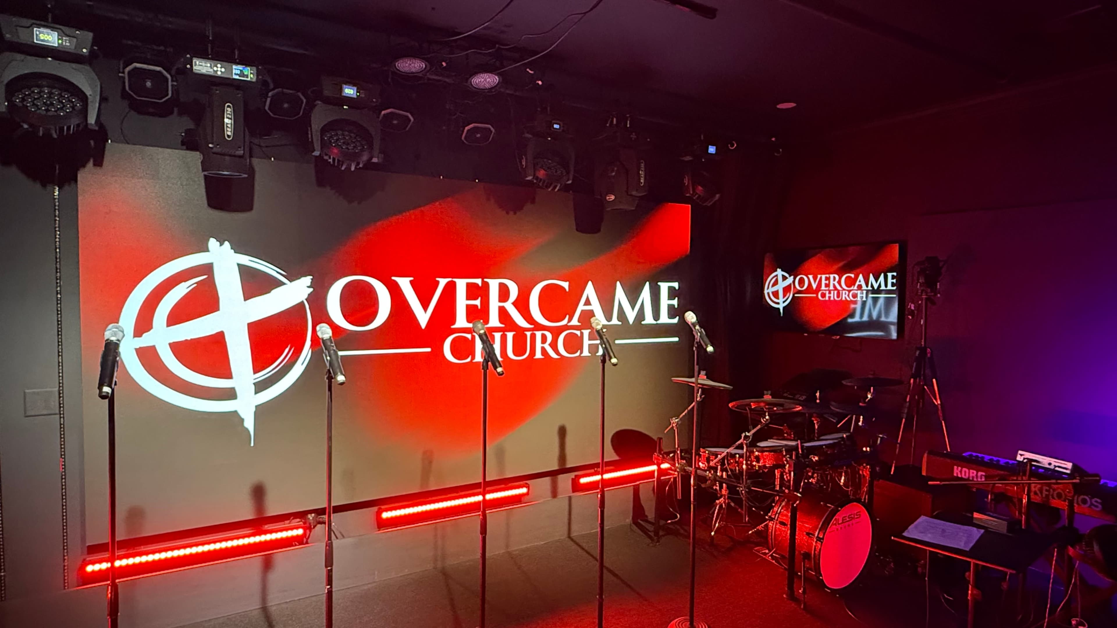 The image shows a stage setup at Overcame Church, featuring microphones and a drum set under colorful stage lighting.