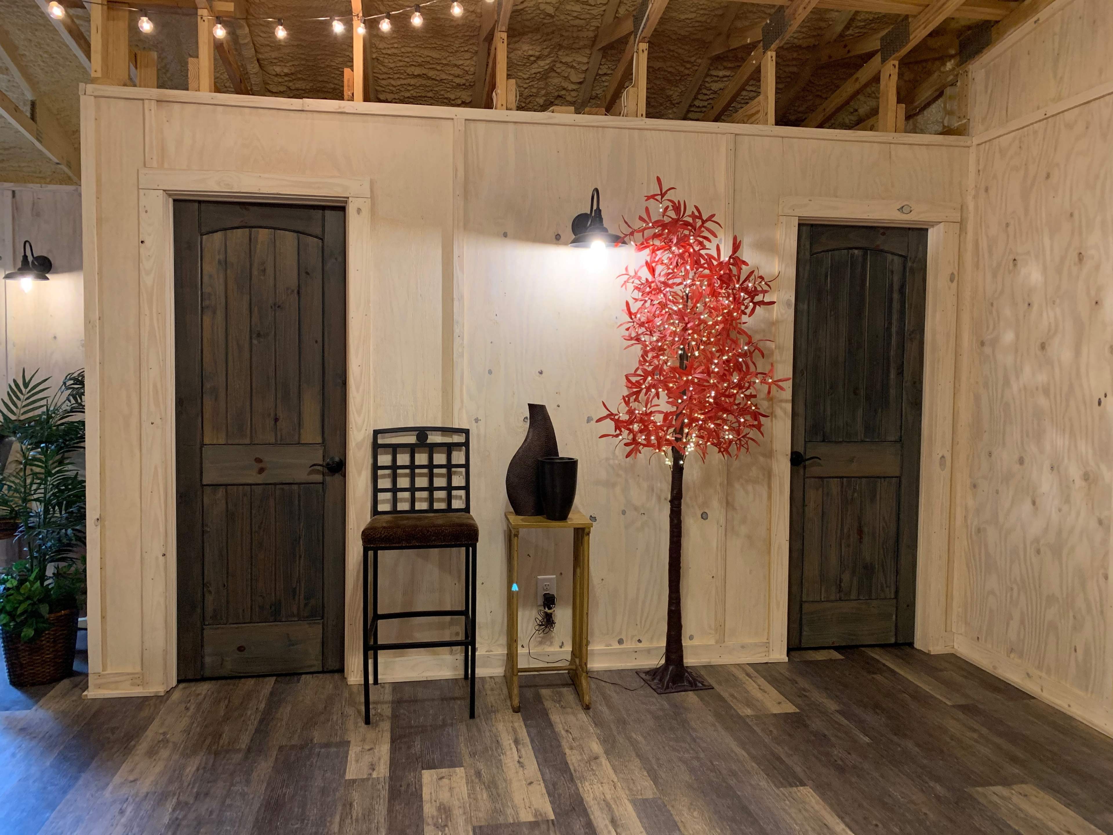 The scene shows a cozy room with two doors, a wooden chair, a tall red tree decoration, and a vase on a small table against a paneled wall.