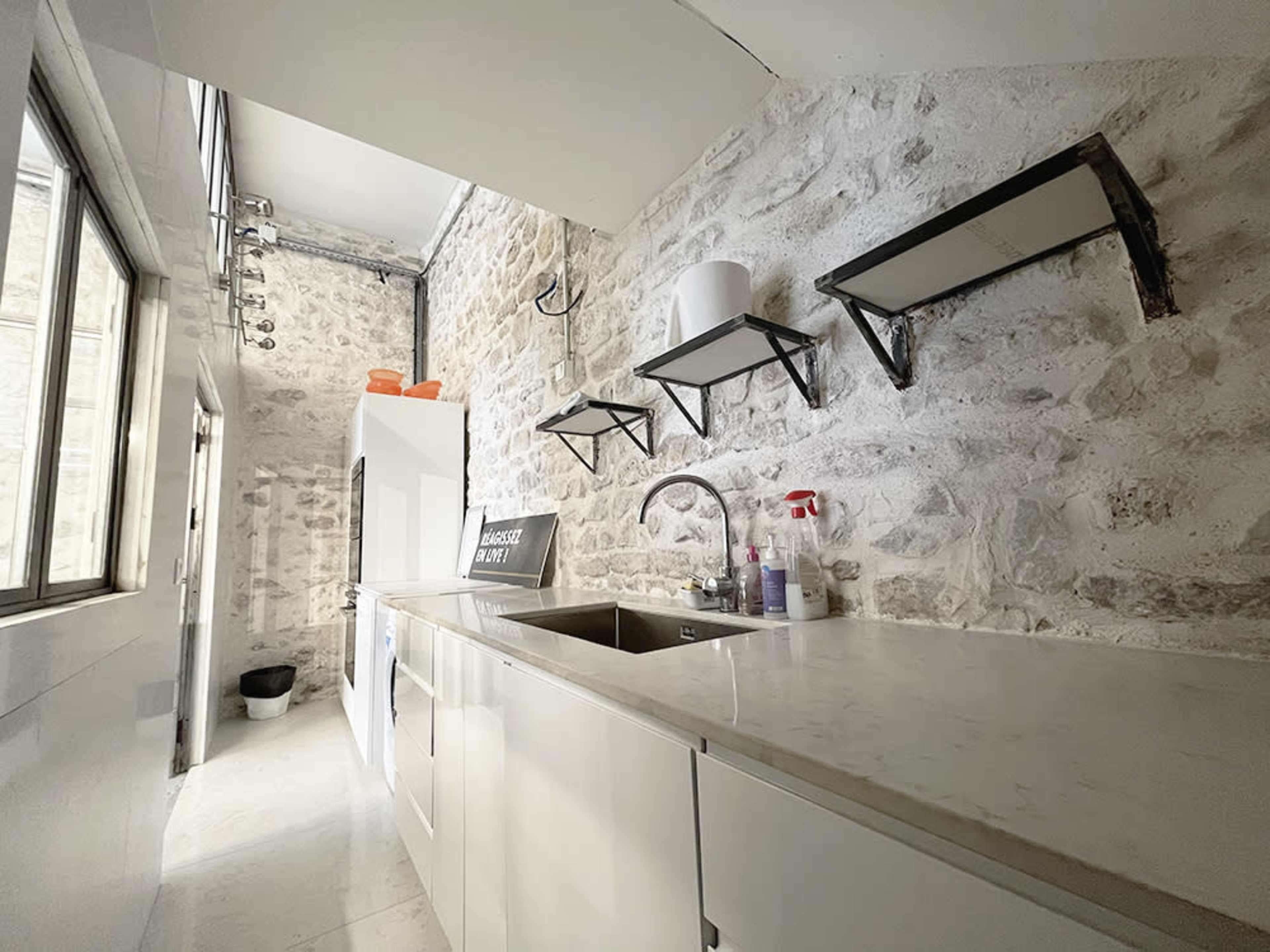 A narrow kitchen with stone walls, a white cabinet, and modern shelves above a sink.