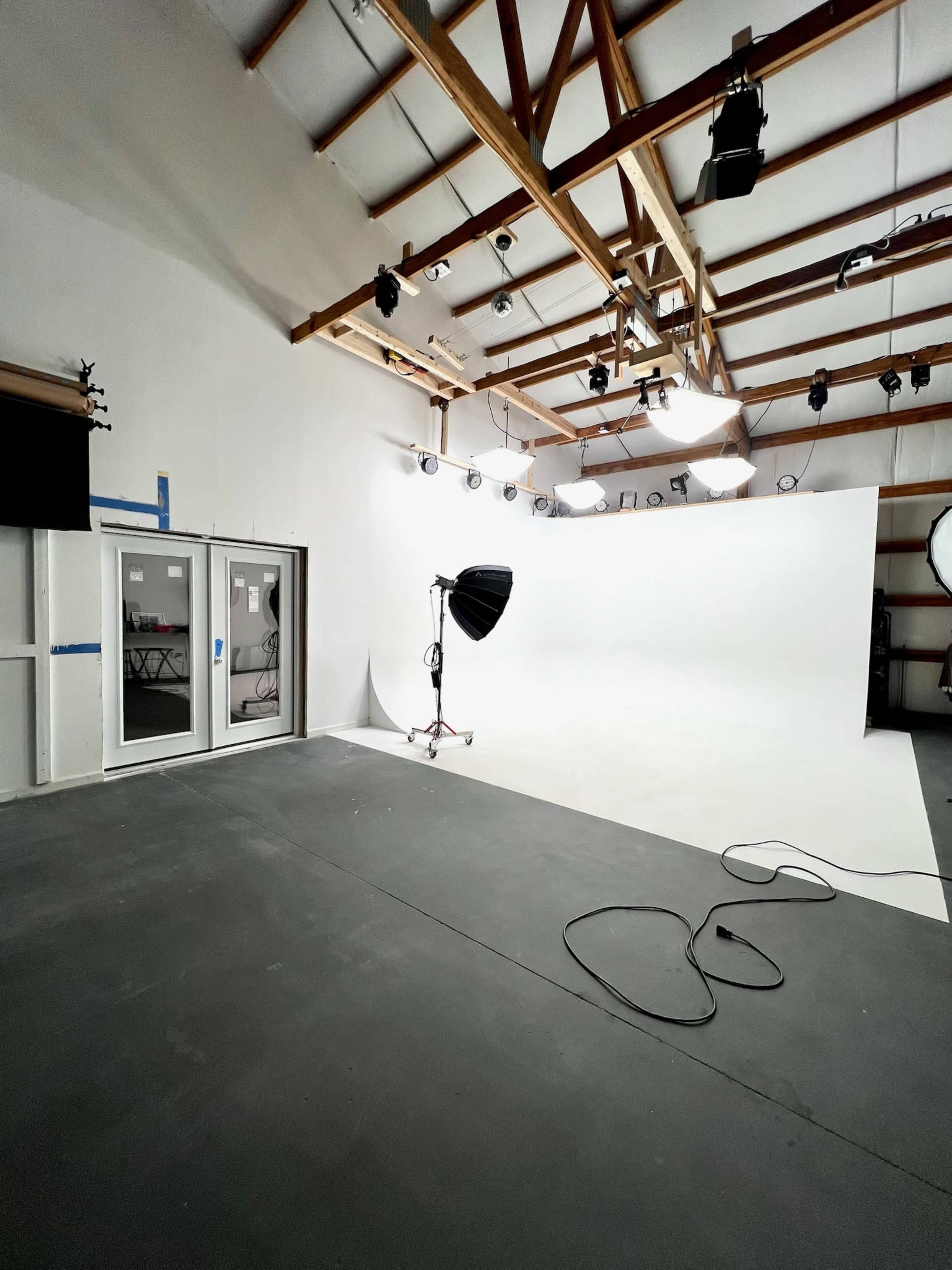 The image shows a photography studio with a white backdrop, studio lights, and a concrete floor.