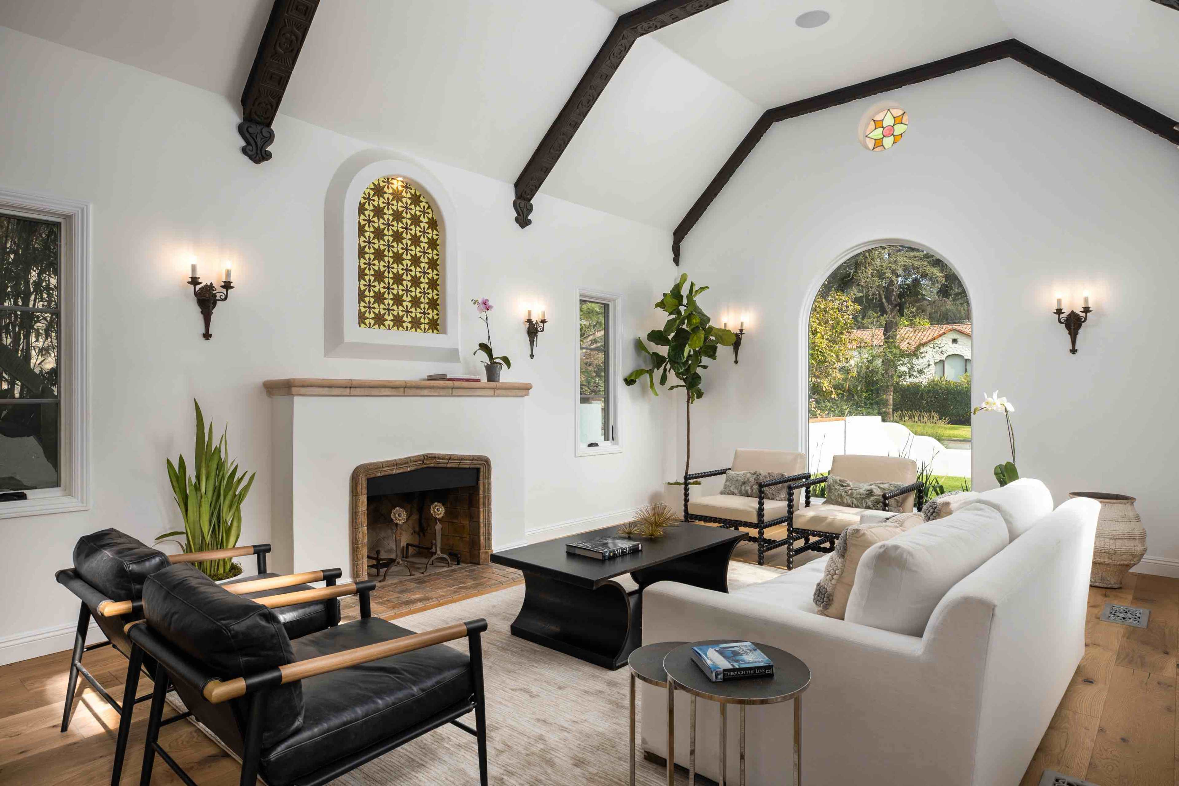 The living room features a bright, spacious area with a white sofa, black chairs, and a fireplace, accented by large windows and vaulted ceilings.