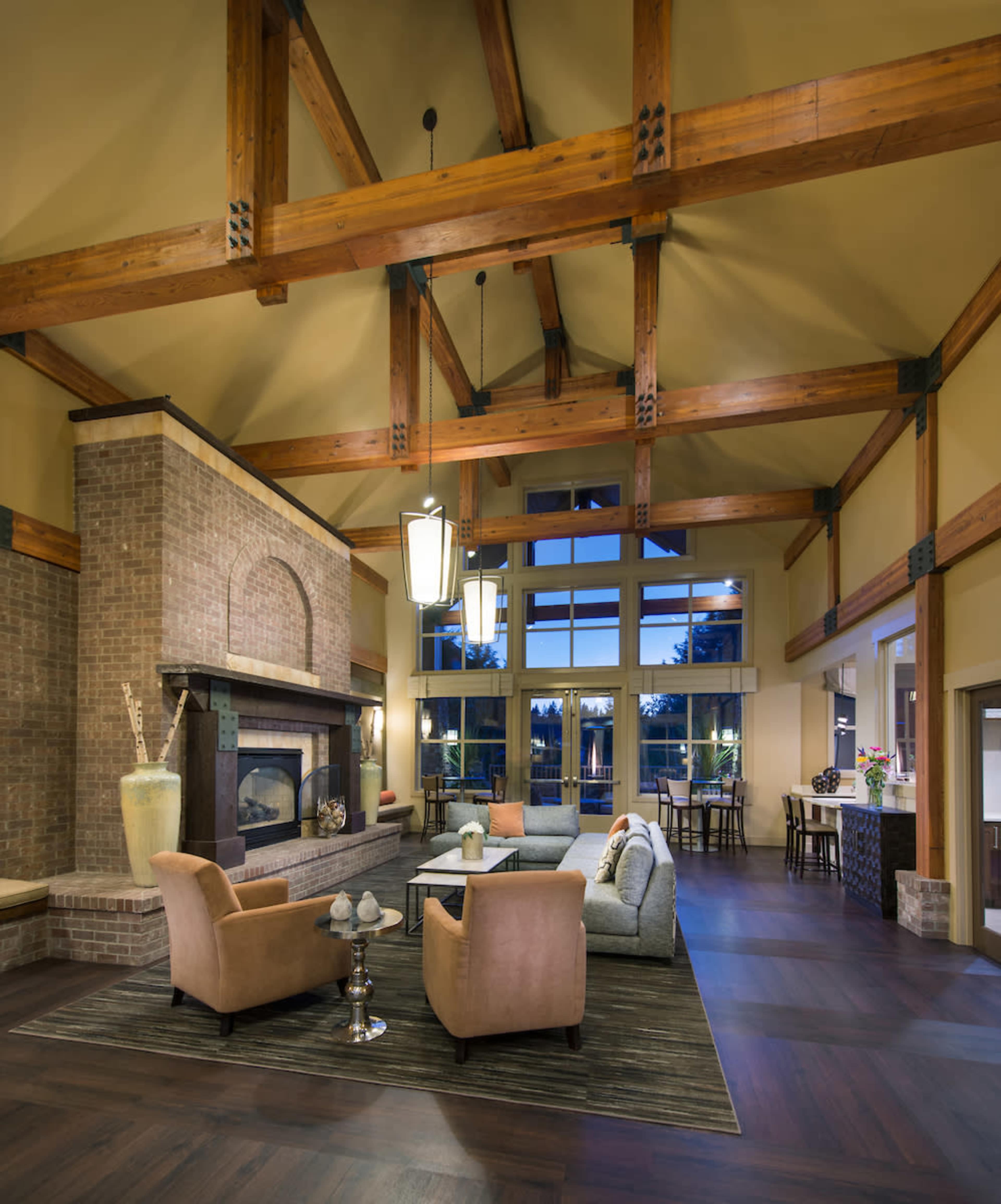 A spacious lounge with a high ceiling, exposed wooden beams, a fireplace, and a seating area arranged around a coffee table.