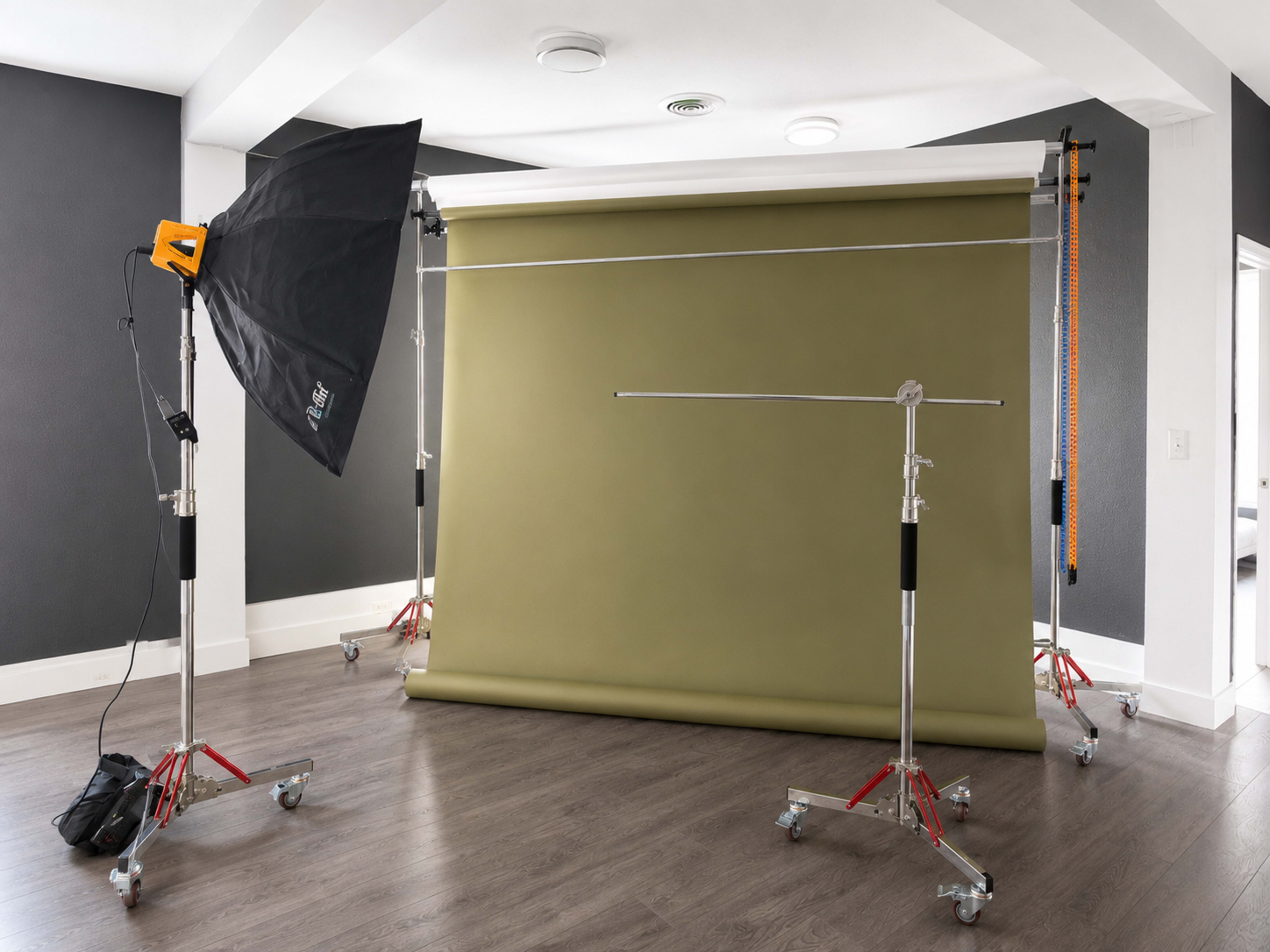 The image shows a photography setup featuring a green backdrop supported by stands, accompanied by a softbox light and various equipment on a wooden floor in a studio-like room.