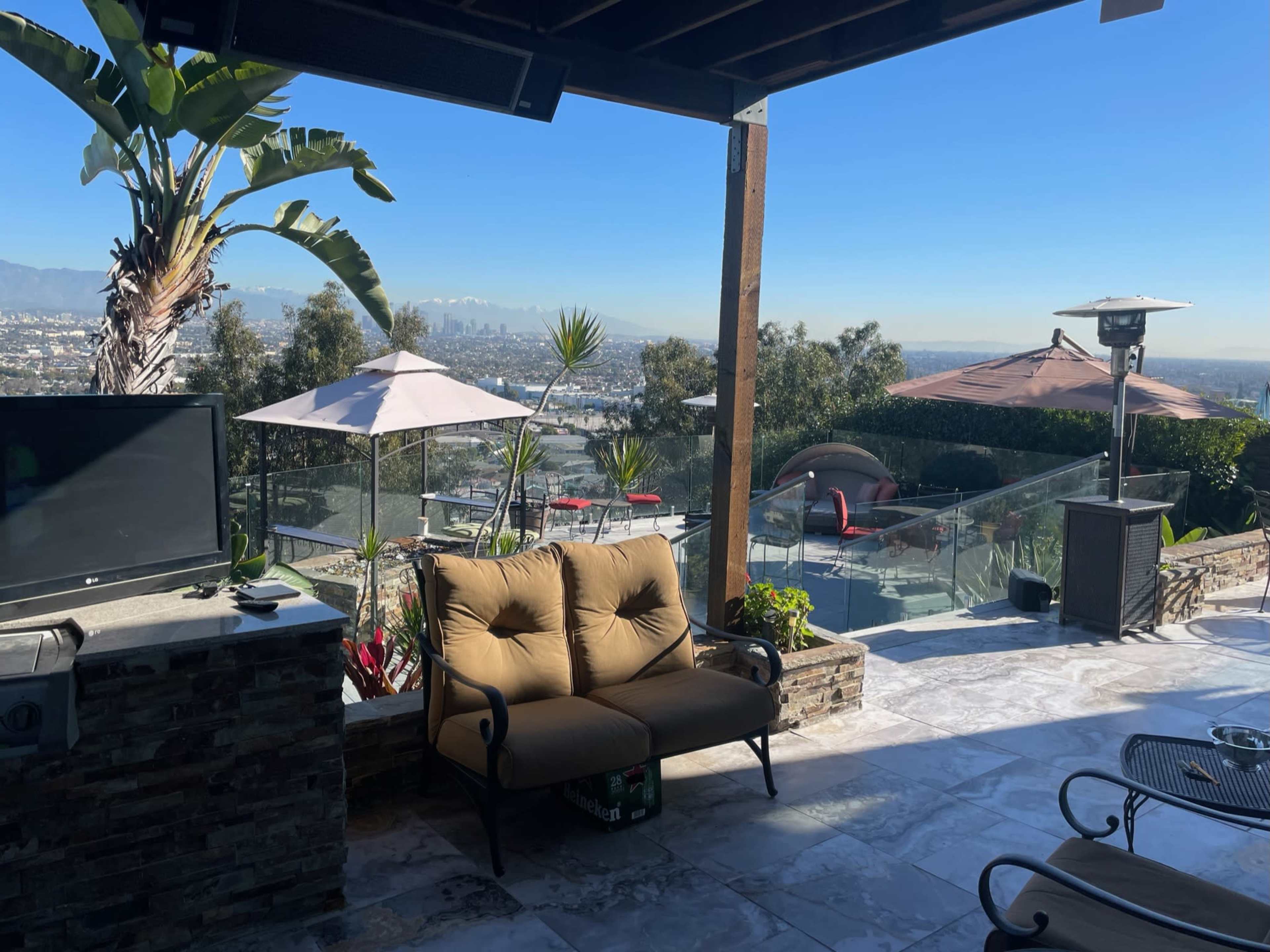 A patio with a couch, outdoor heaters, and a view of a city skyline and mountains in the background.