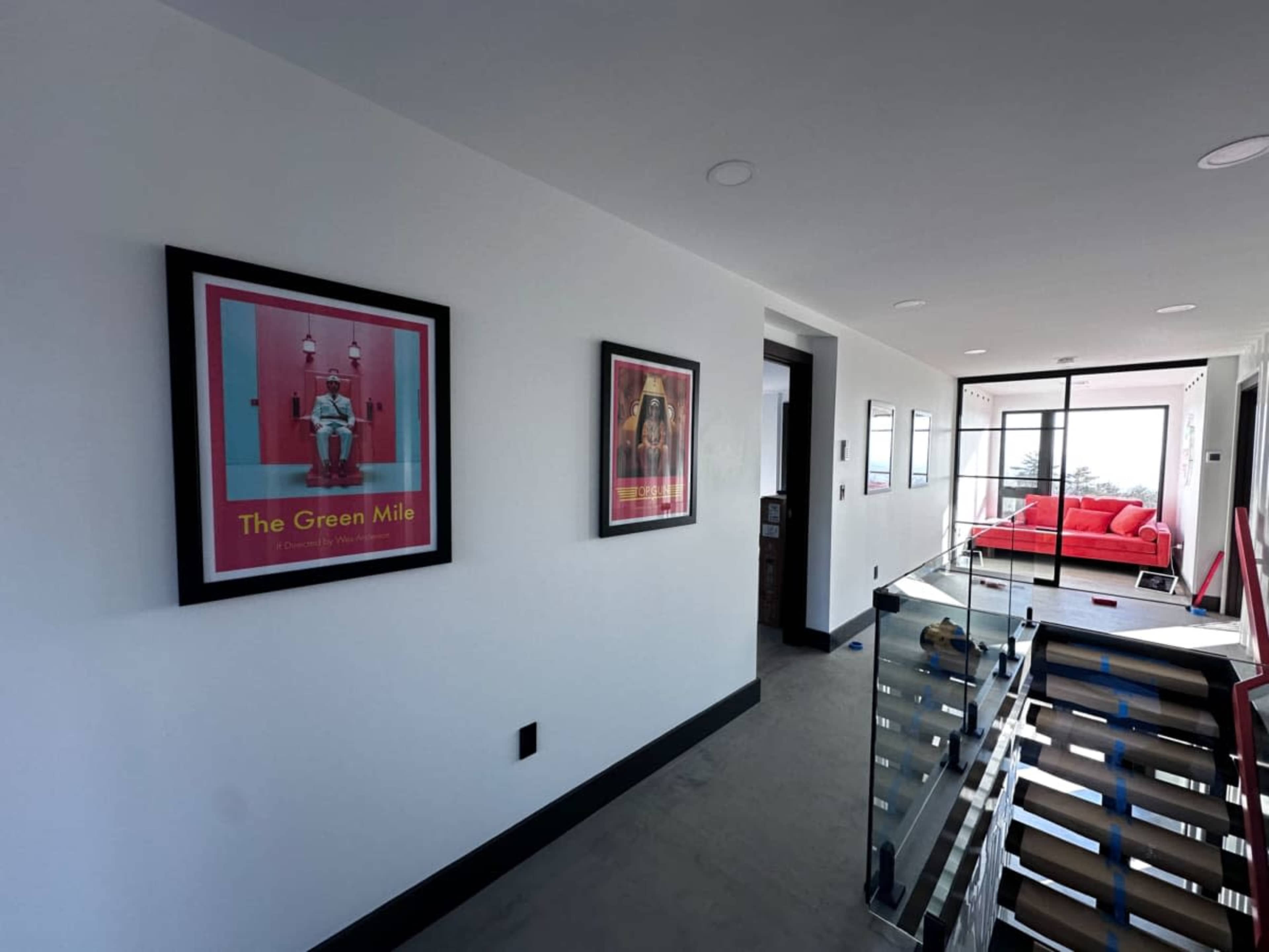 A hallway features framed posters of movies on the white walls, with a red couch visible in the background.