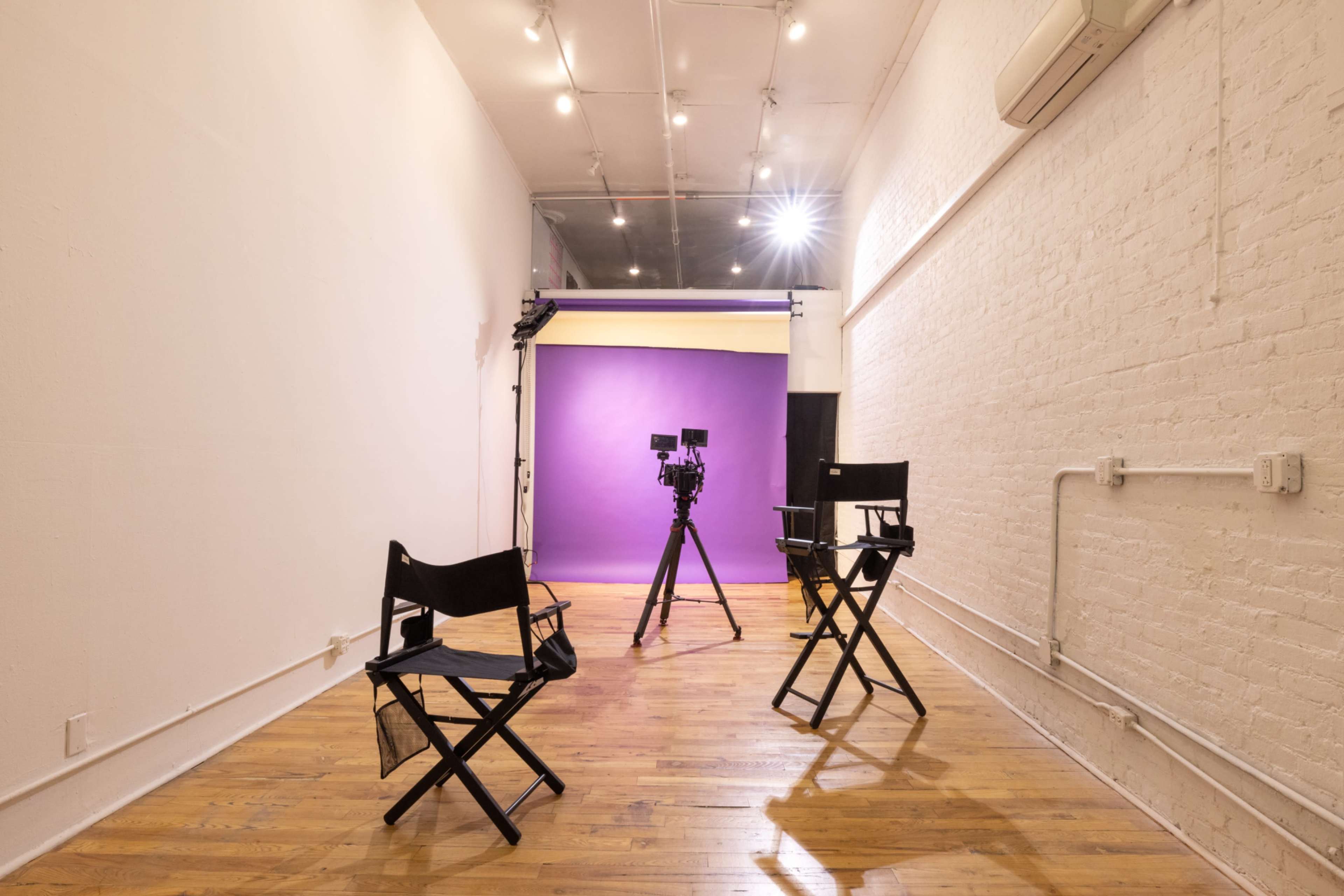 A minimalist studio features three black director's chairs facing a camera setup in front of a purple backdrop.
