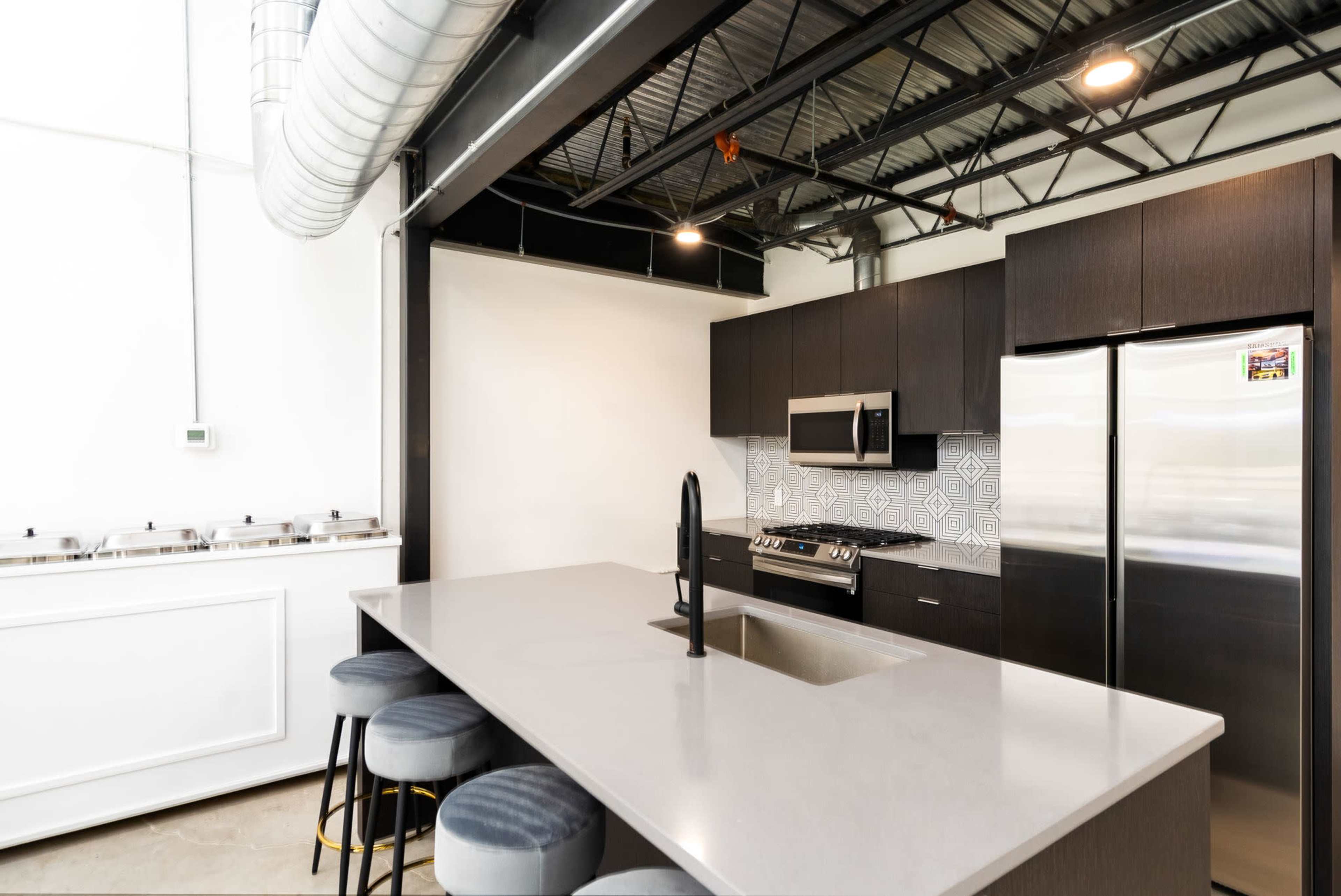 A modern kitchen with dark cabinetry, stainless steel appliances, a large island with a sink, and bar stools.