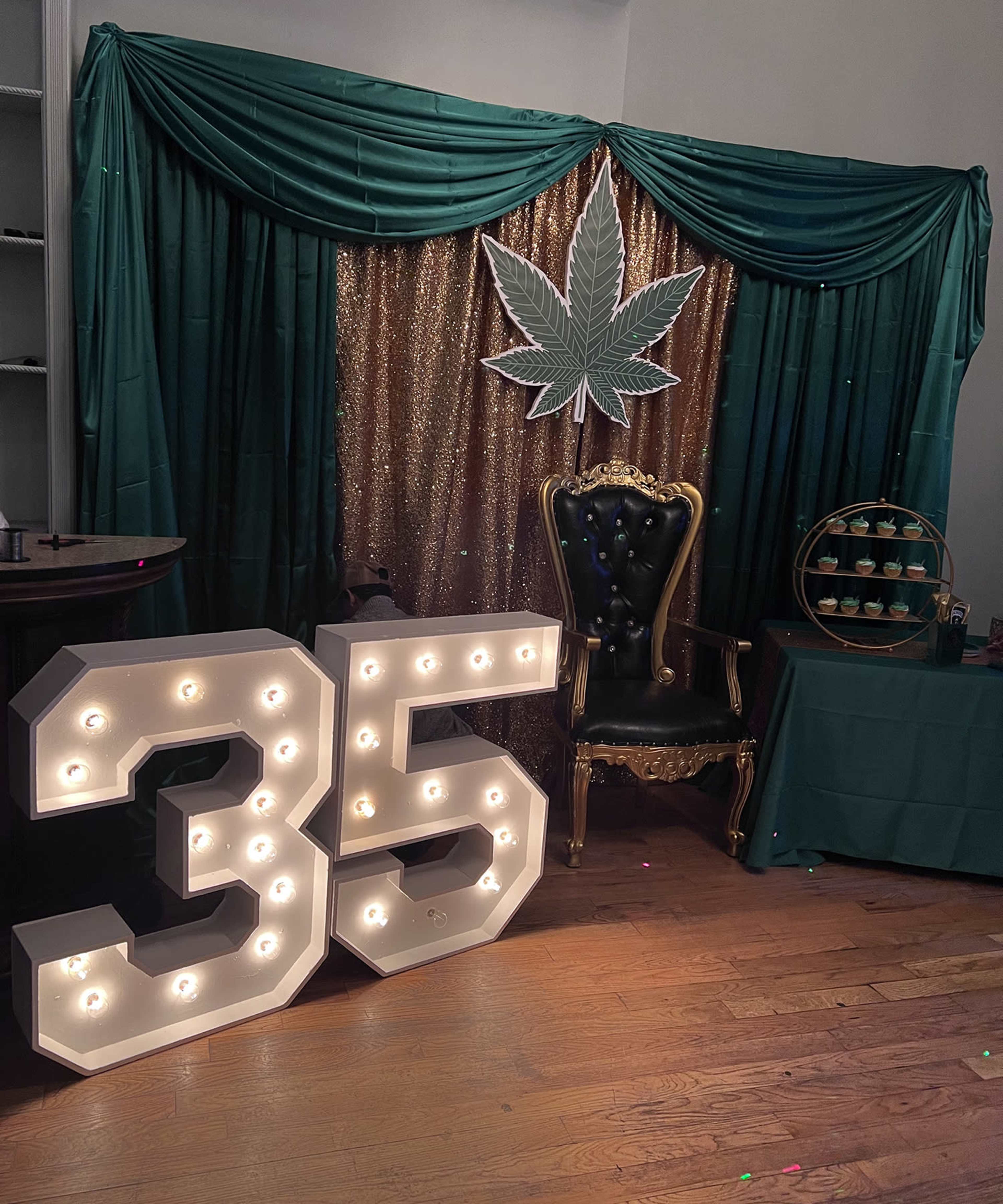 The scene features a decorative backdrop with green and gold elements, highlighting a large illuminated "35" and a cannabis leaf design, along with a plush chair and a dessert display.