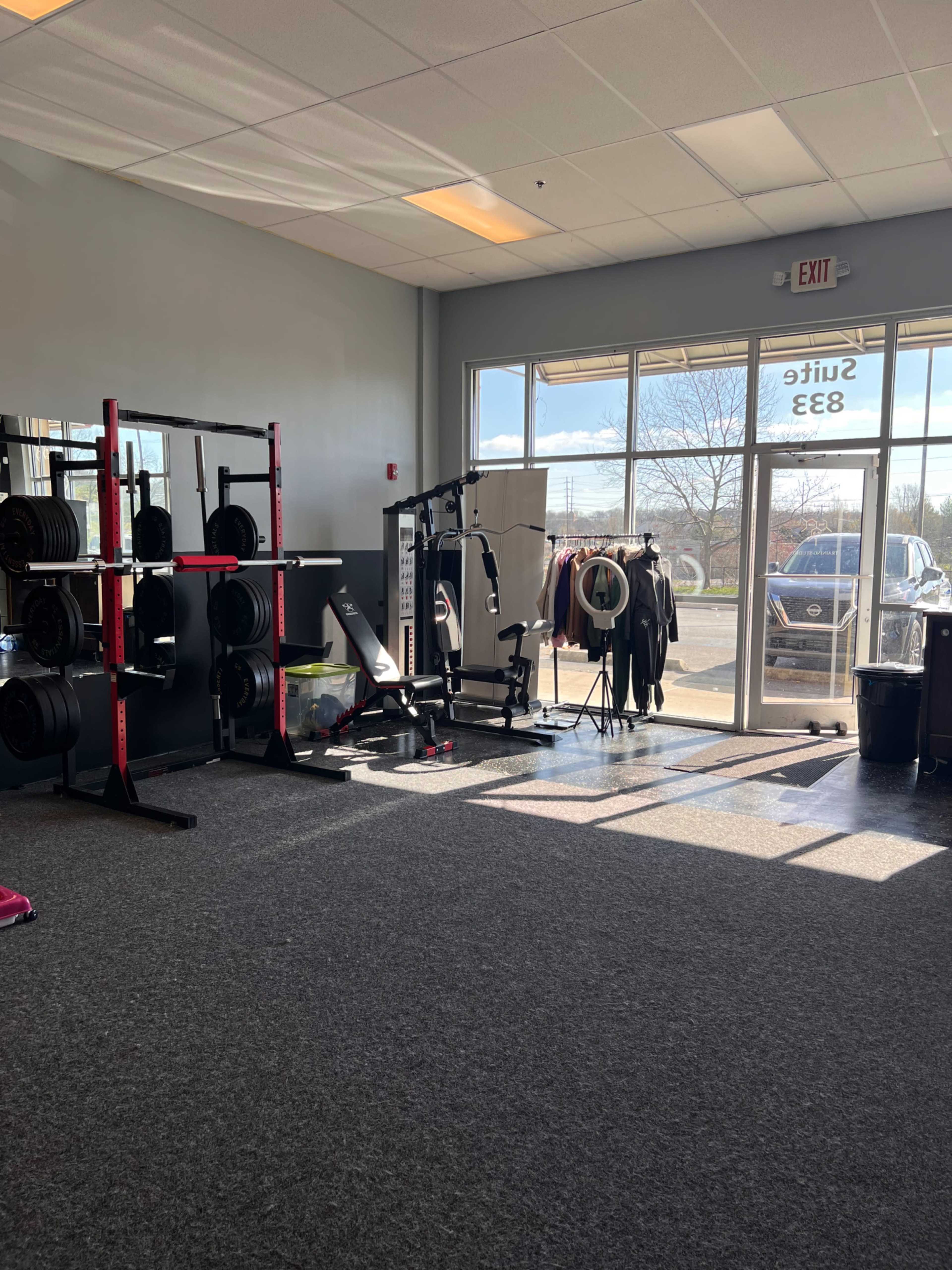 A gym interior with weightlifting equipment on one side and a large window offering outdoor views.