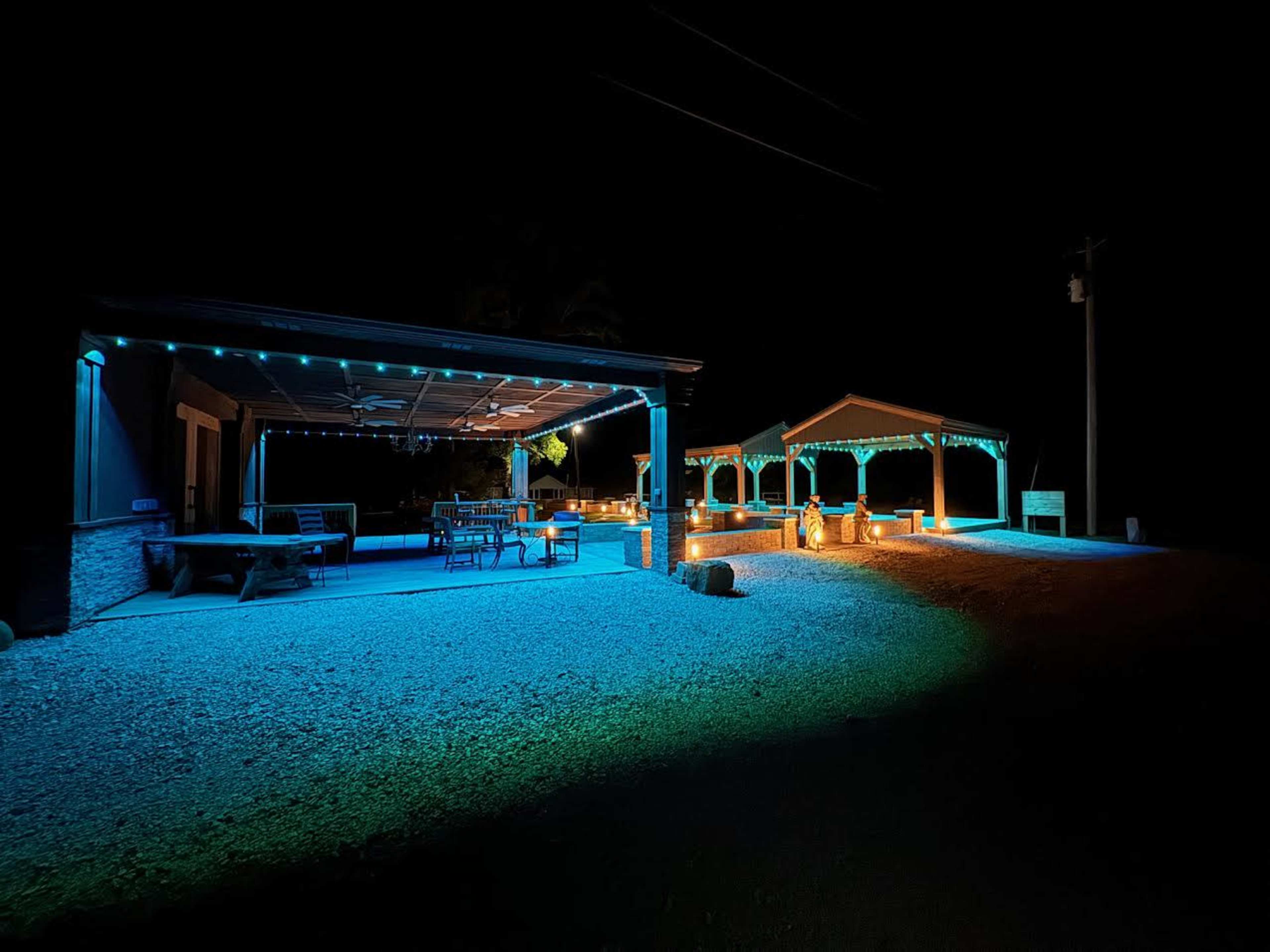 A well-lit outdoor space at night features a covered patio with furniture and a separate gazebo area.