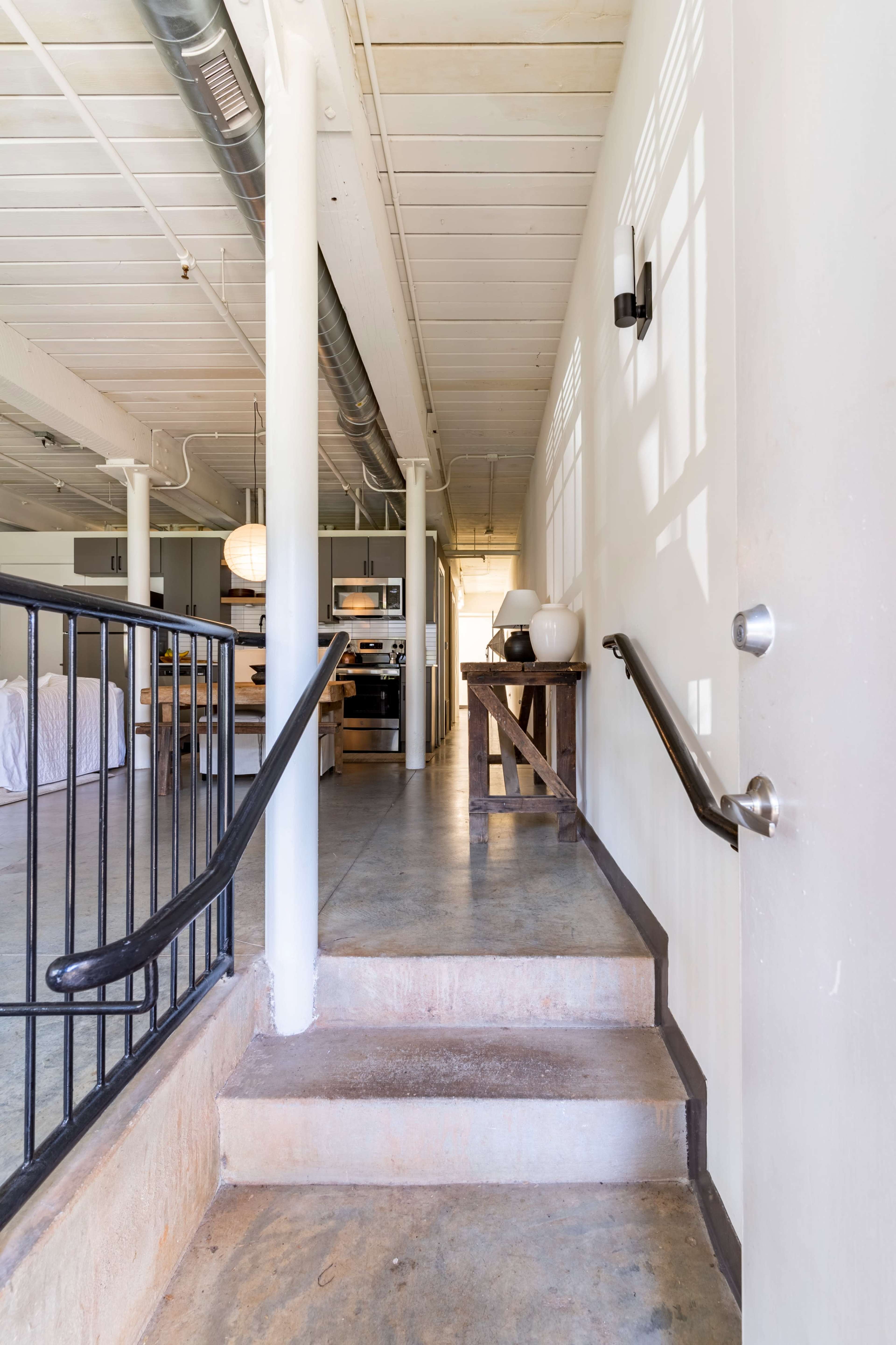 The image shows a staircase leading up from a concrete floor to a well-lit, modern interior space.