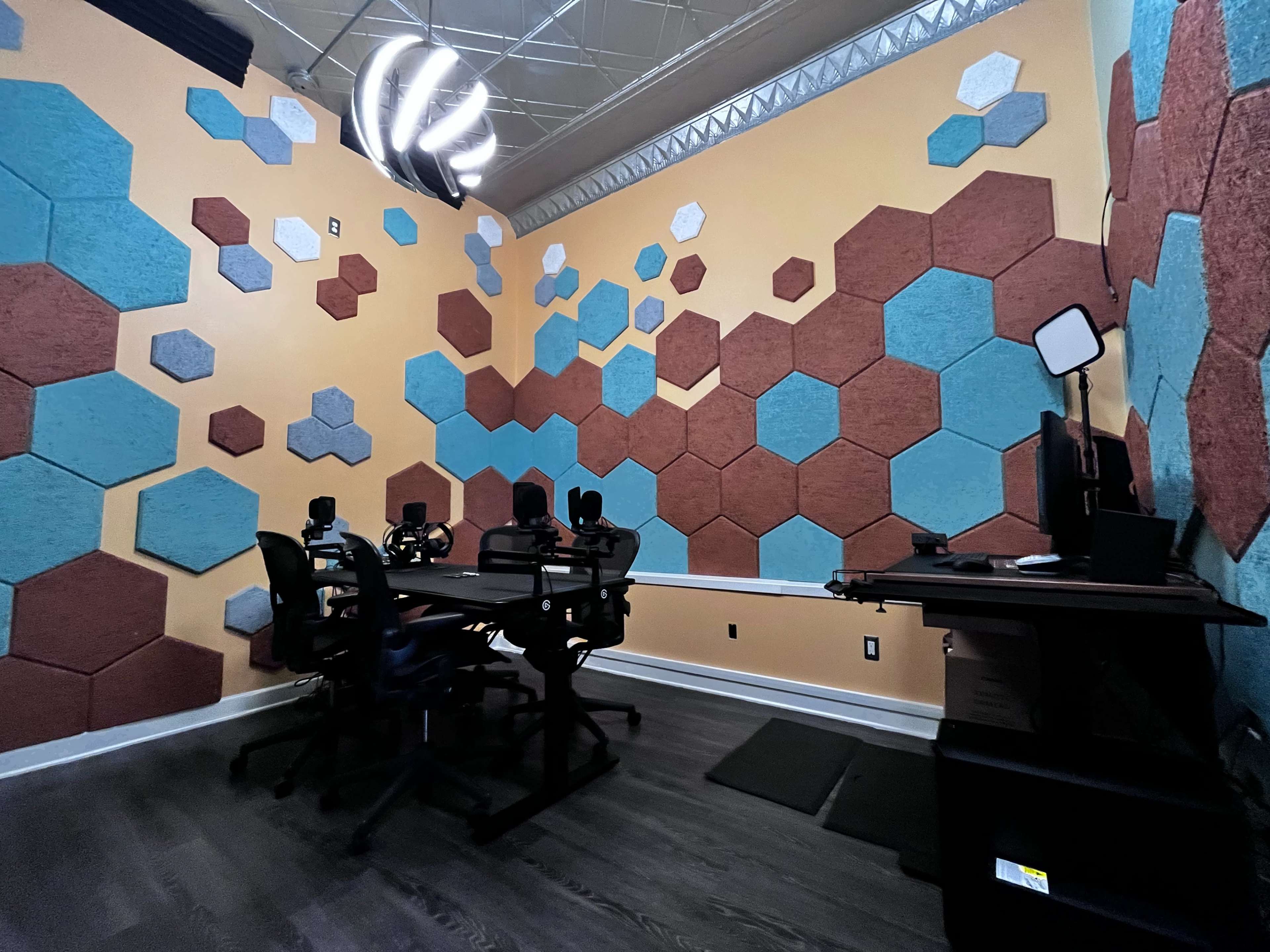The room features a modern design with hexagonal wall panels in various colors and a central table equipped with multiple chairs and computer setups.