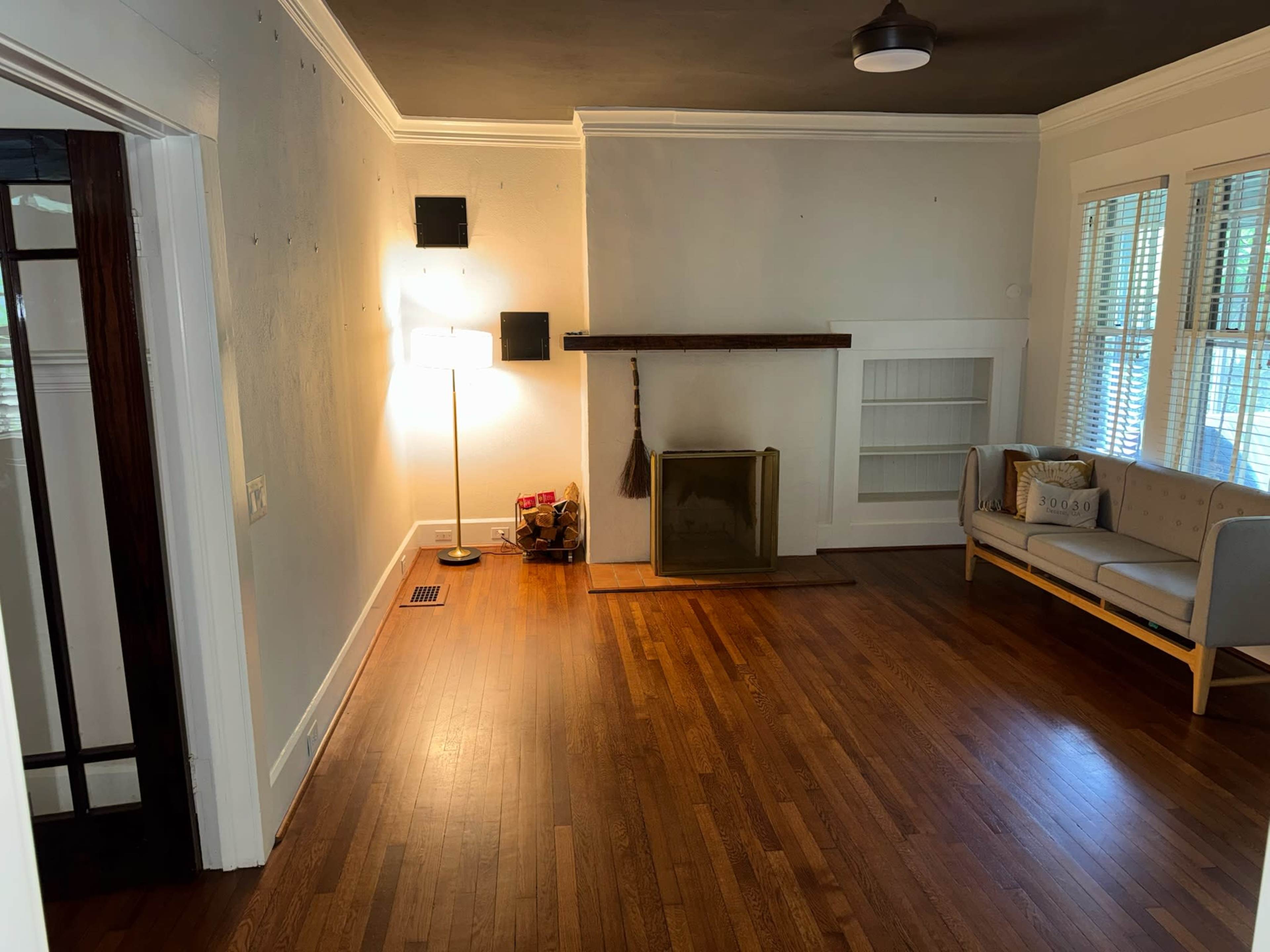 The image shows a living room with a wooden floor, a couch, a lamp, and a fireplace against a wall with built-in shelves.