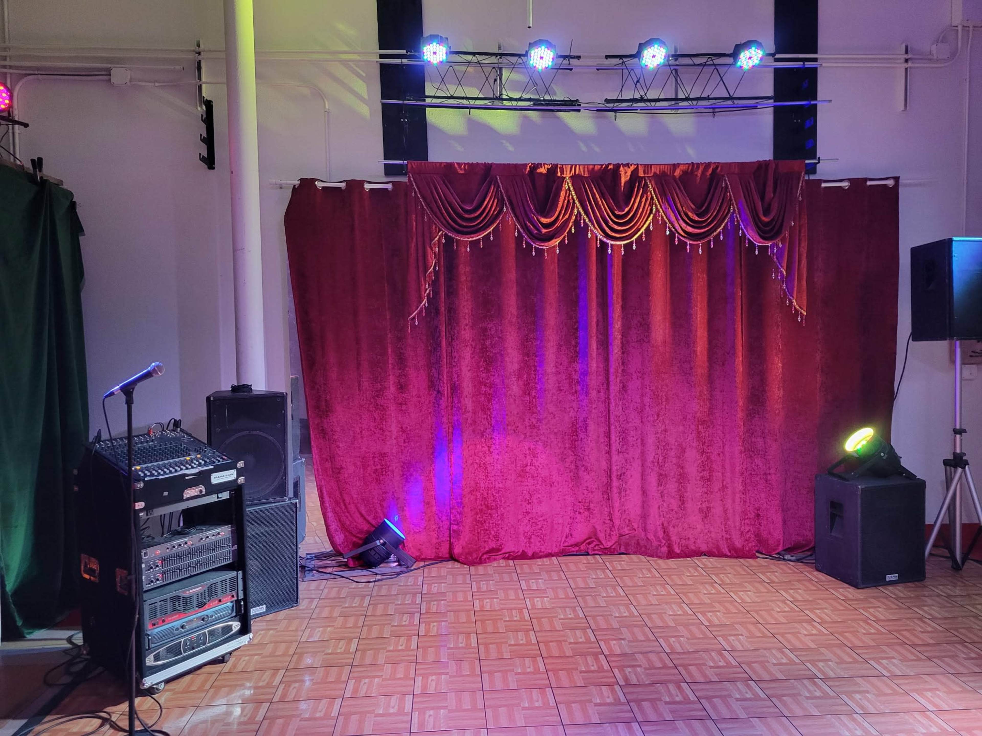 The image shows a stage area with a red curtain draped at the front, flanked by audio equipment and stage lights.