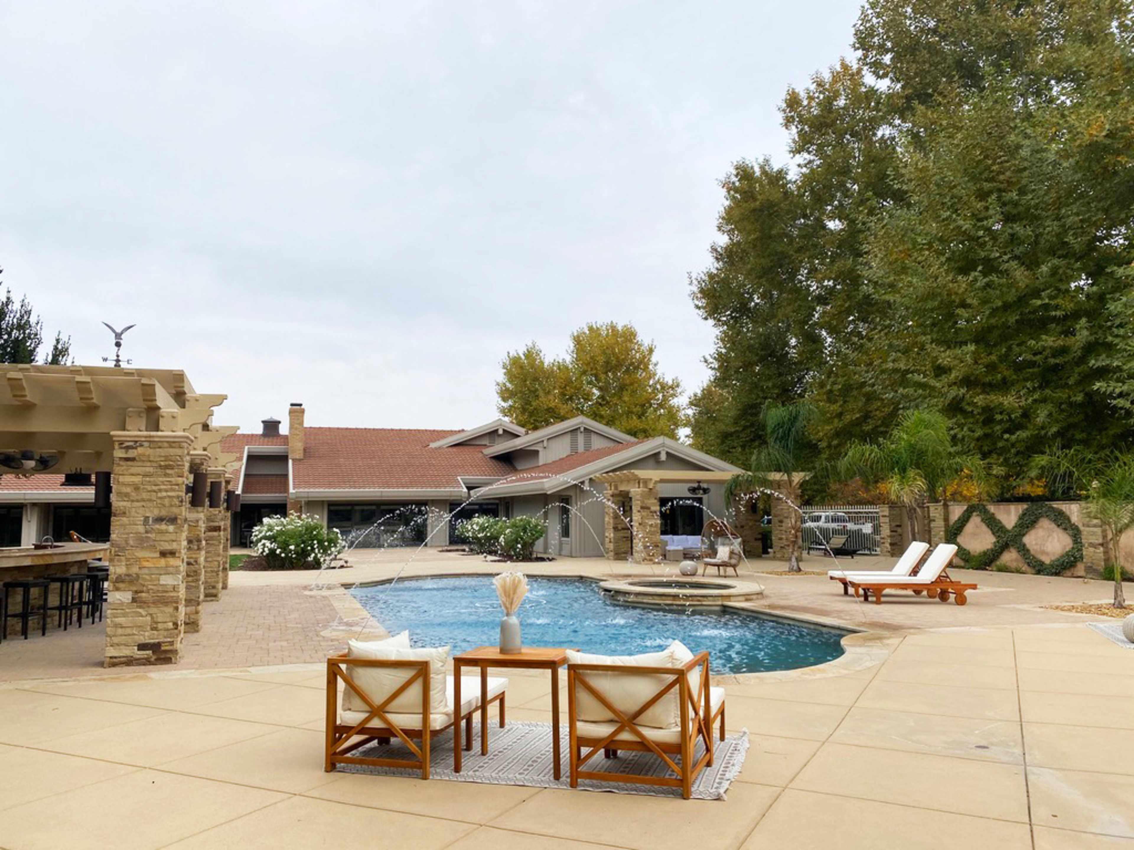 The image shows a landscaped backyard with a swimming pool, lounge chairs, and a house with a tiled roof in the background.