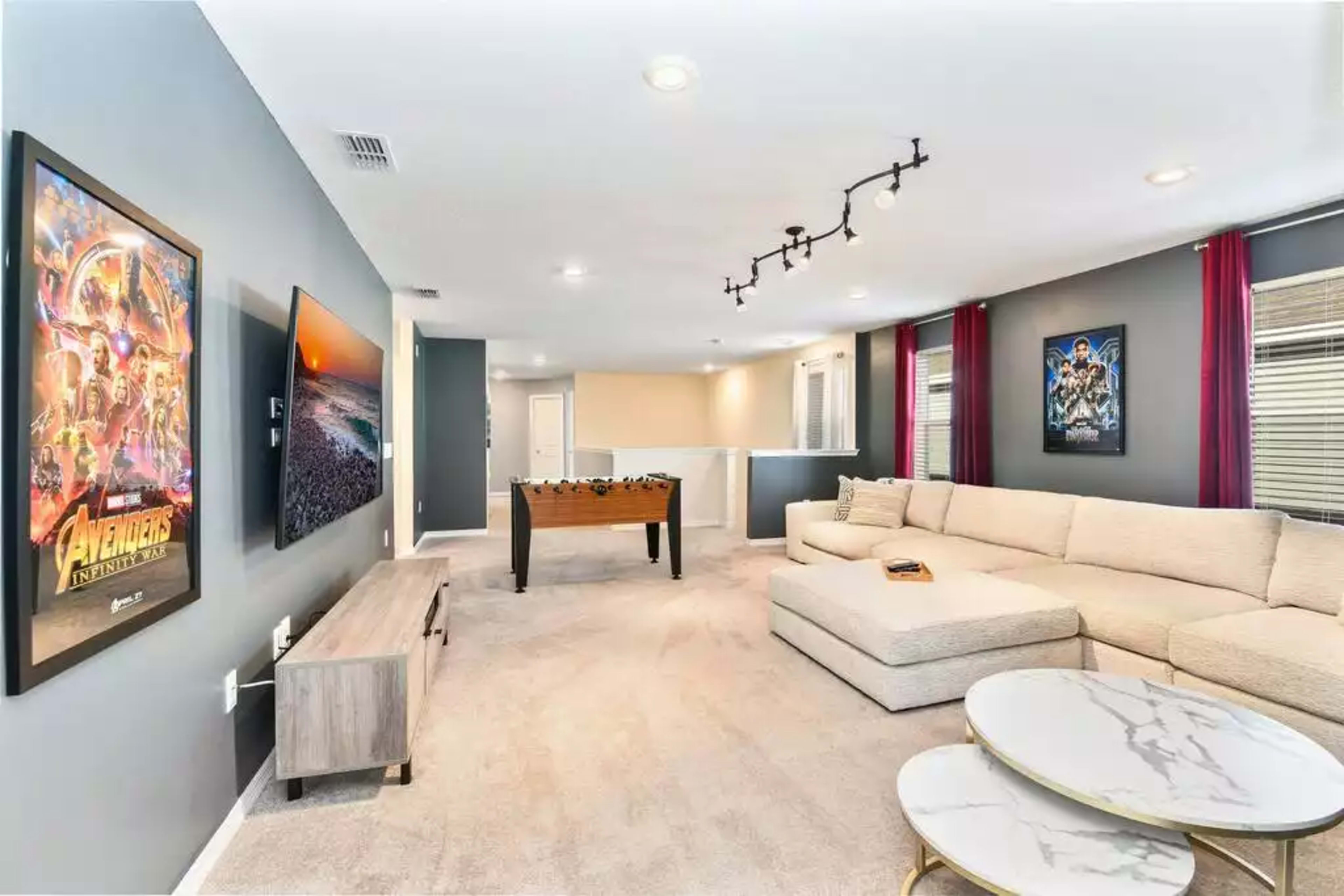A modern living room with a sectional sofa, a foosball table, and framed movie posters on the walls.