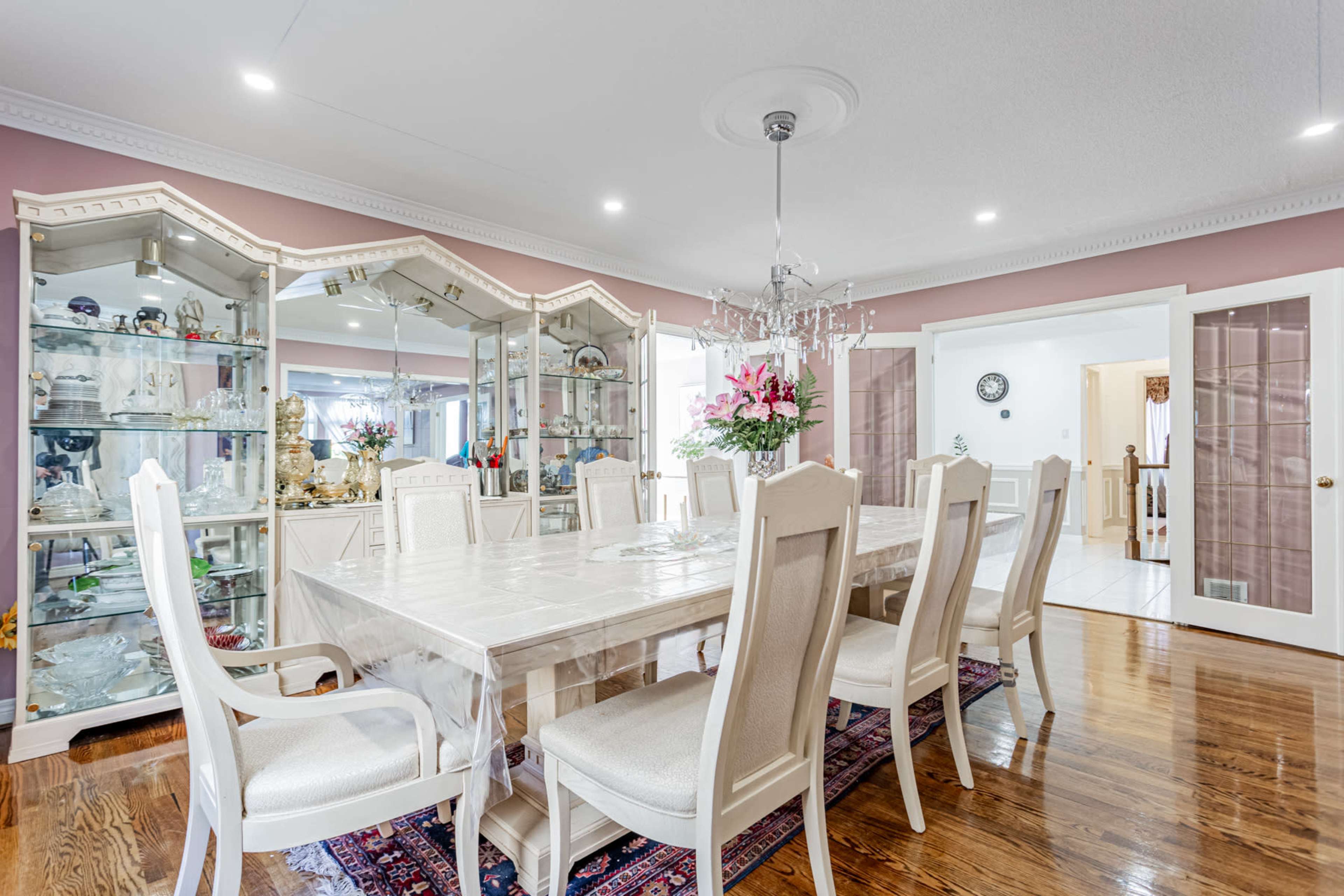 A spacious dining room with a large table surrounded by chairs, a chandelier overhead, and display cabinets filled with decorative items along the walls.