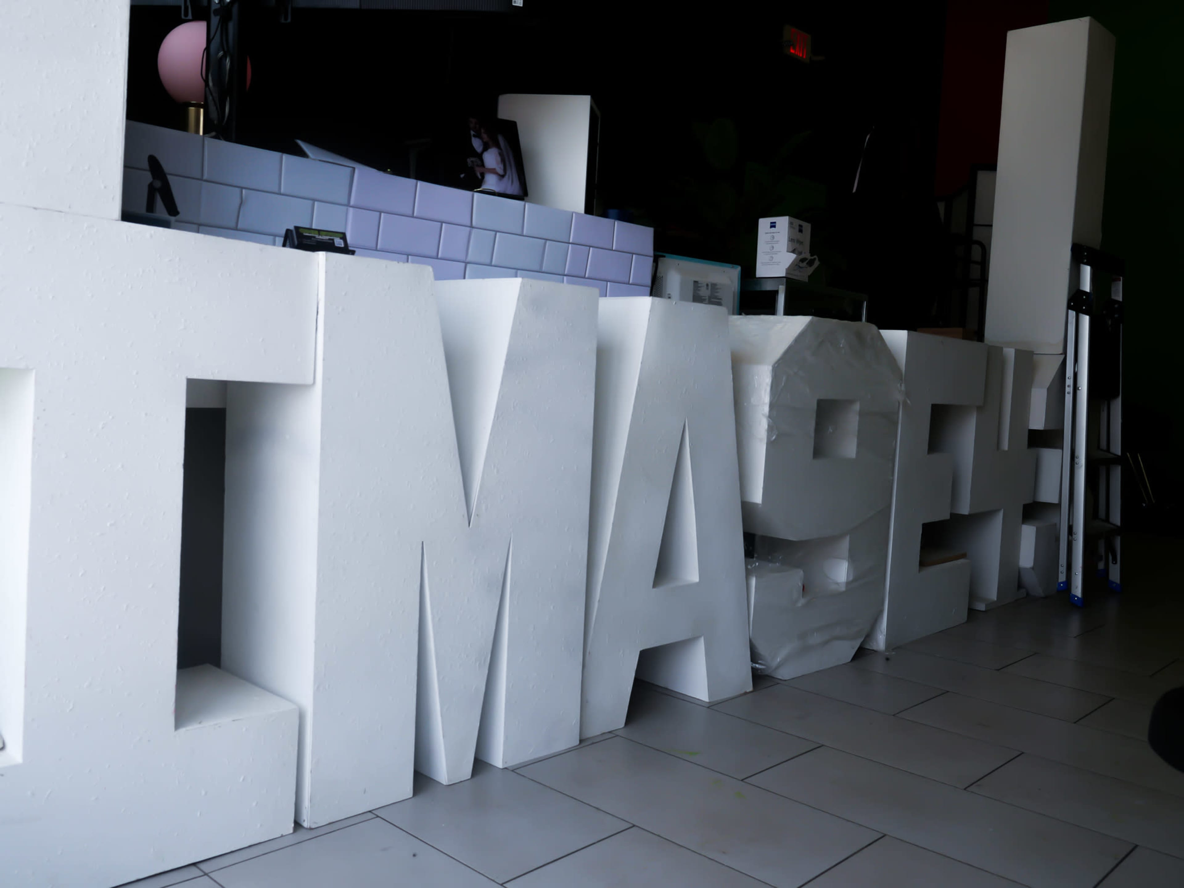 A row of large, white letters spelling "IMAGINE" is positioned on a tiled floor inside a commercial space.