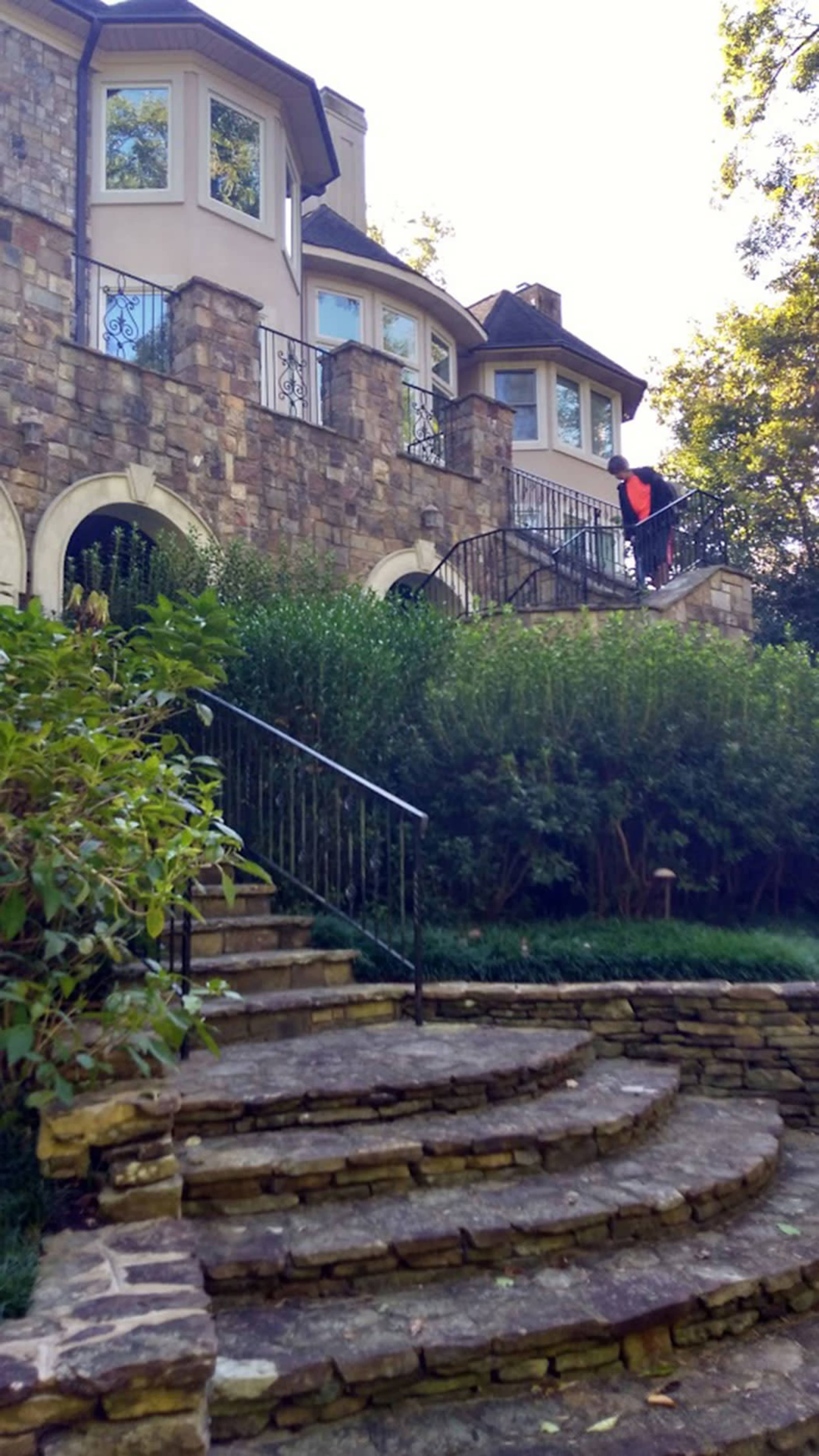 A stone staircase leading up to a house with multiple large windows and a man in an orange vest tending to the yard.