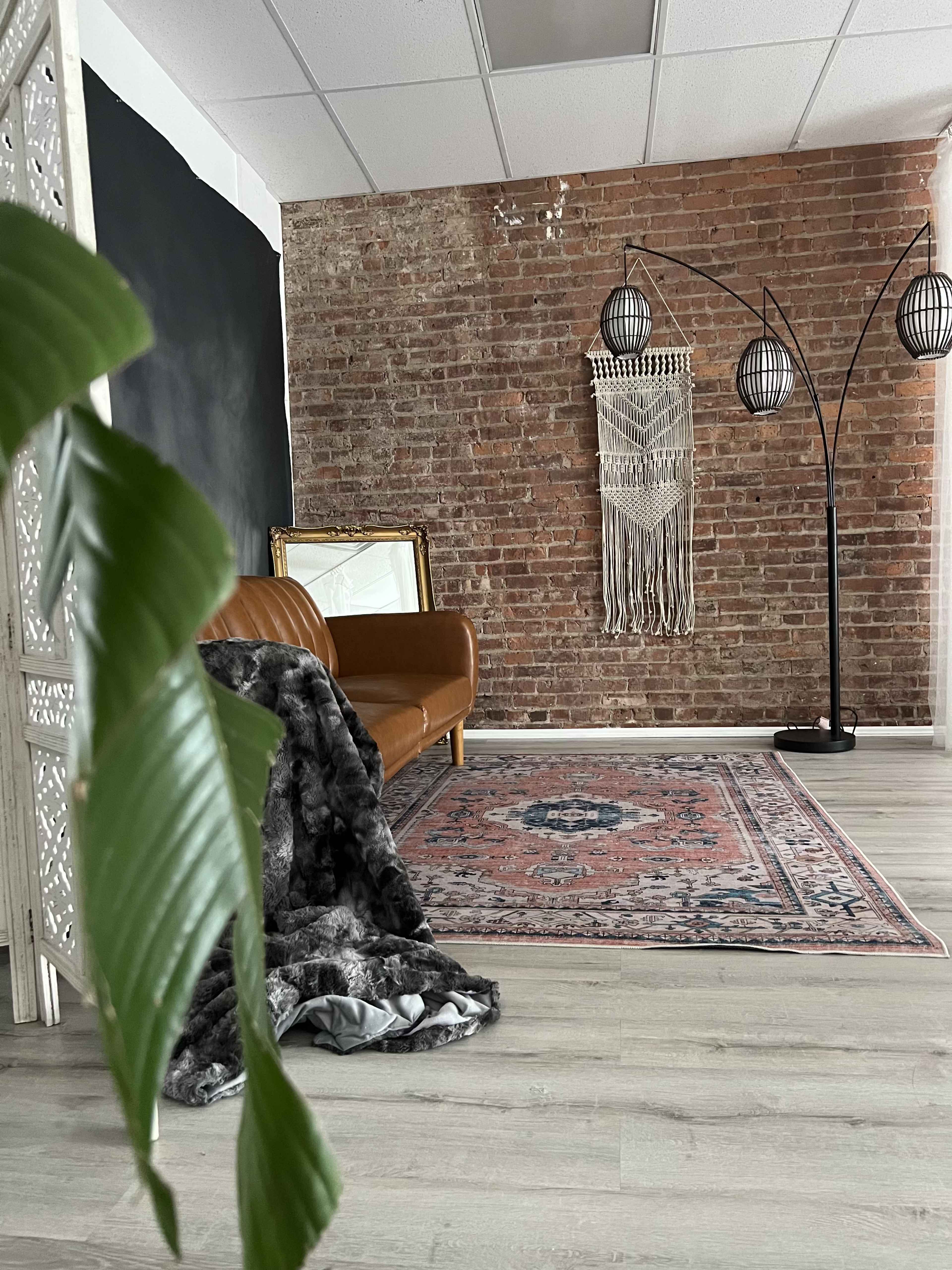 The scene features a leather couch, a patterned rug, and a decorative wall hanging in a room with exposed brick walls and a floor lamp.
