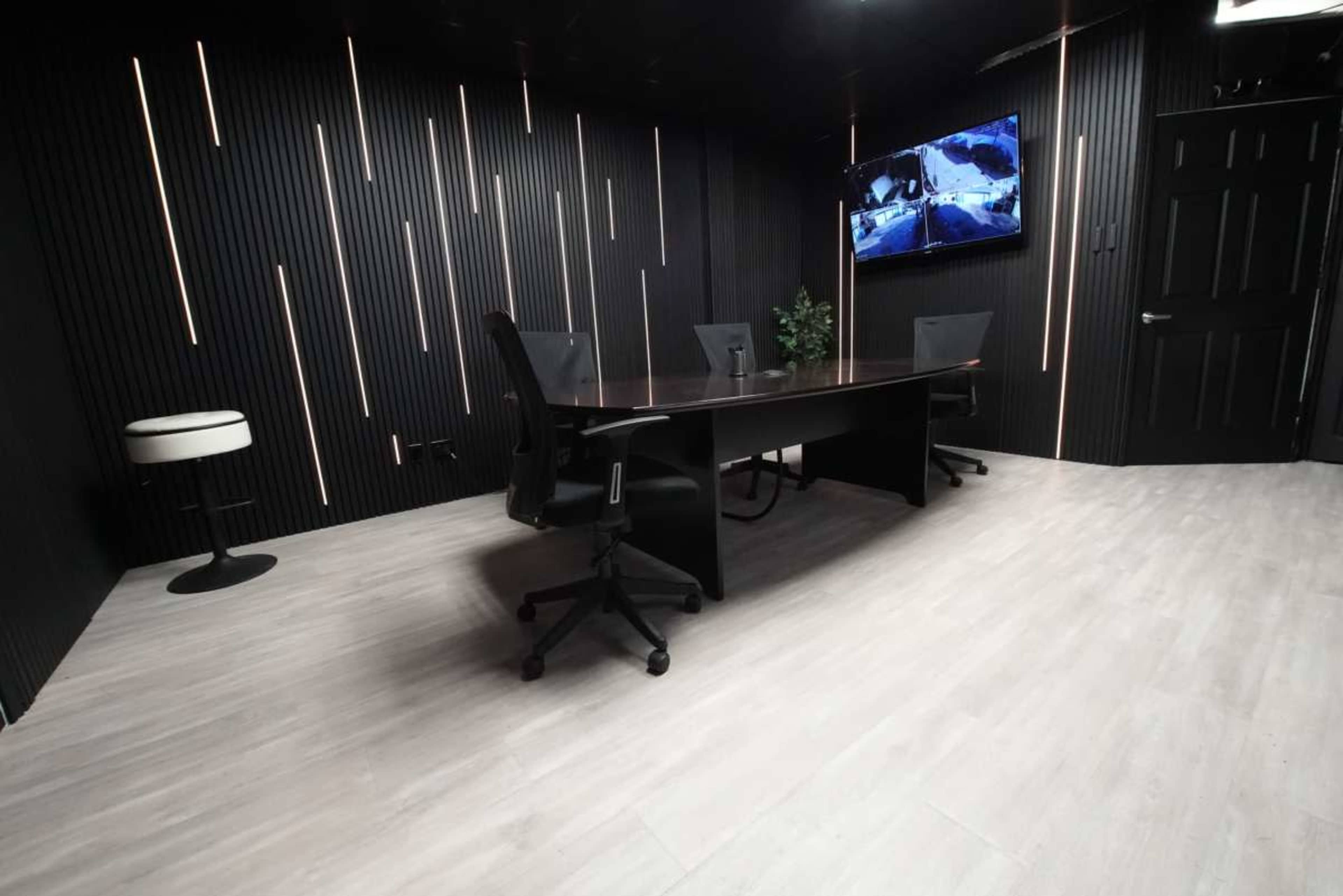 A modern conference room features a dark, vertically striped wall, a large table surrounded by chairs, and a television mounted on the wall.
