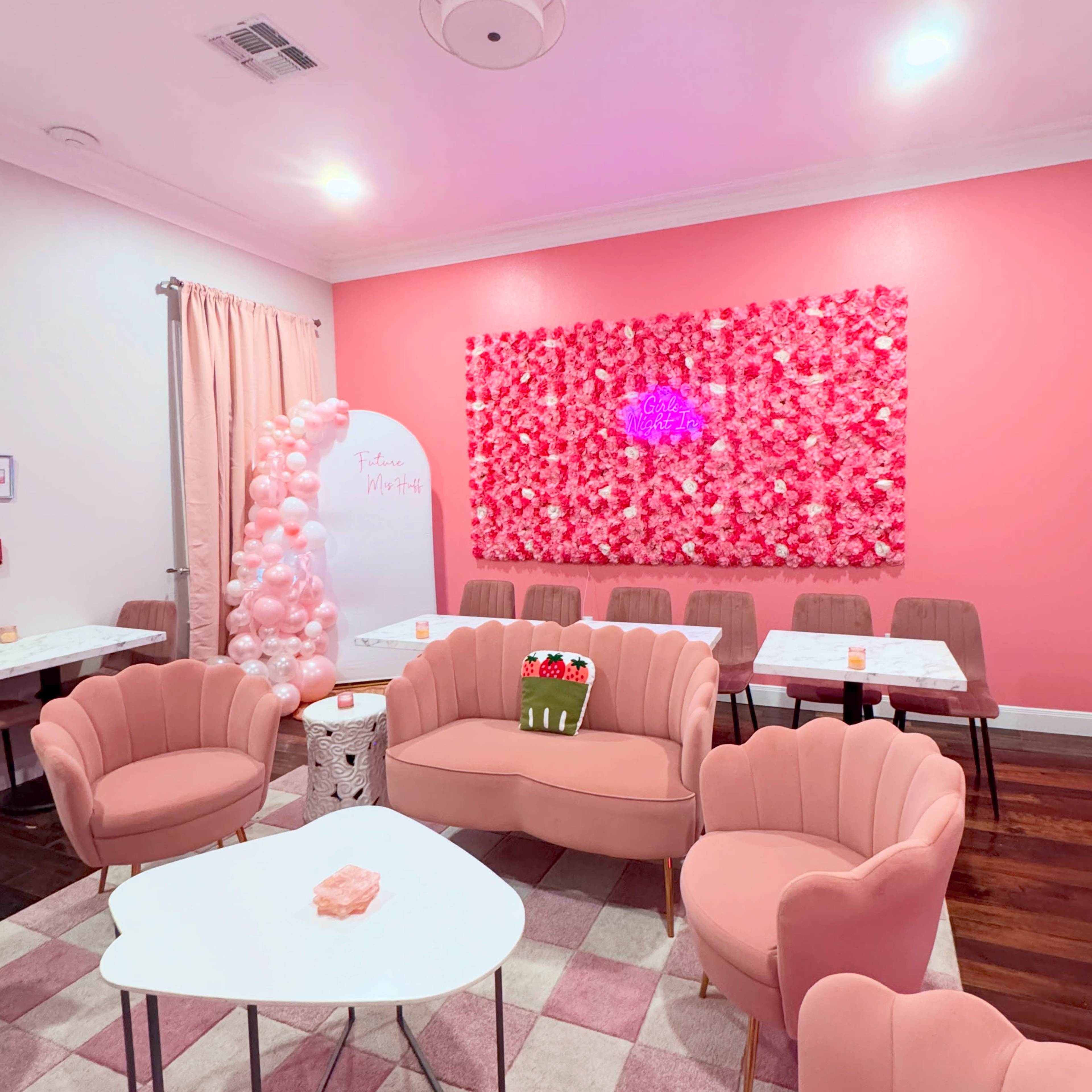The image features a pink-themed room with floral wall decor, several pink chairs, and tables arranged for a gathering.