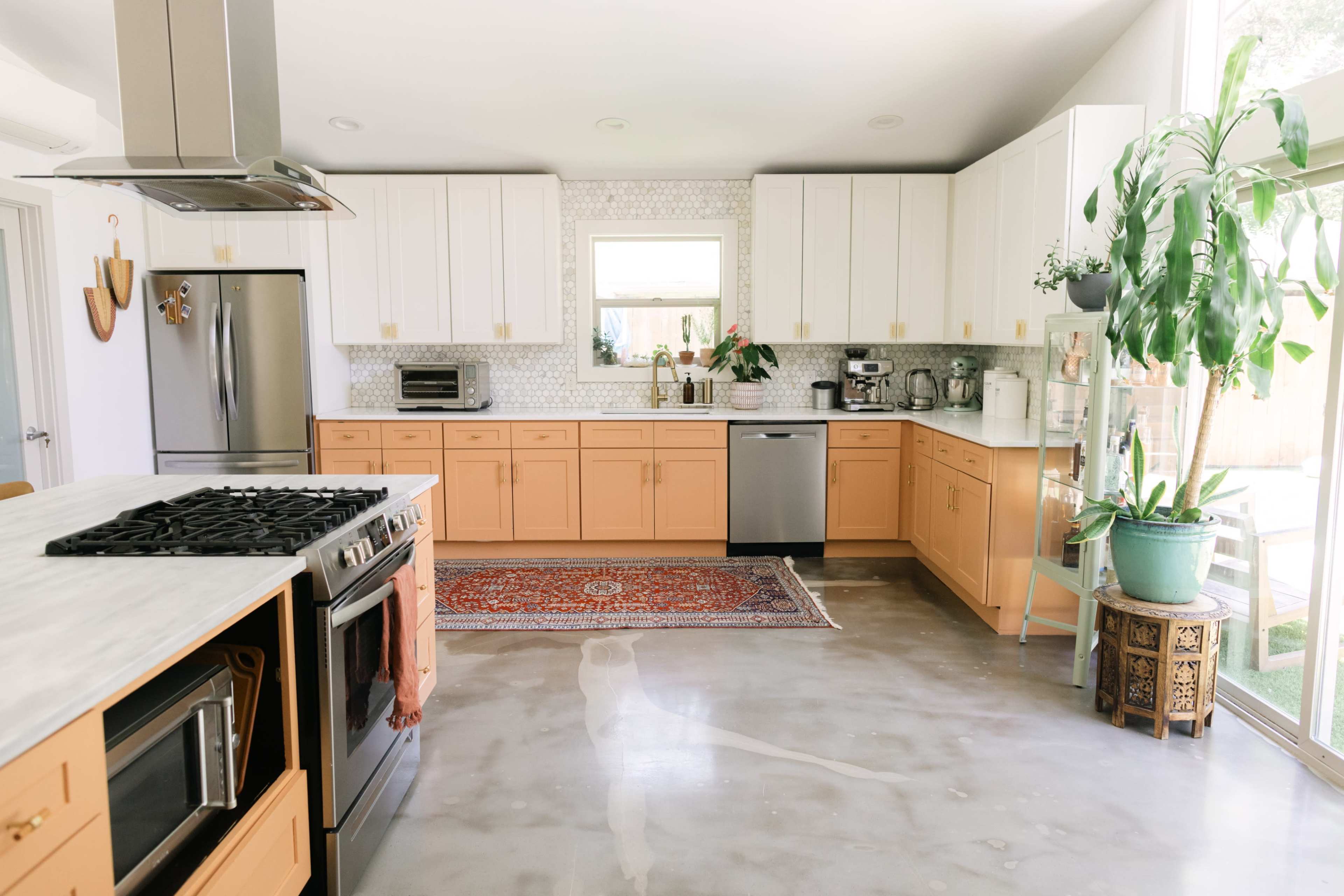 A bright kitchen features beige cabinets, a marble countertop, stainless steel appliances, and a central island with a gas stove.