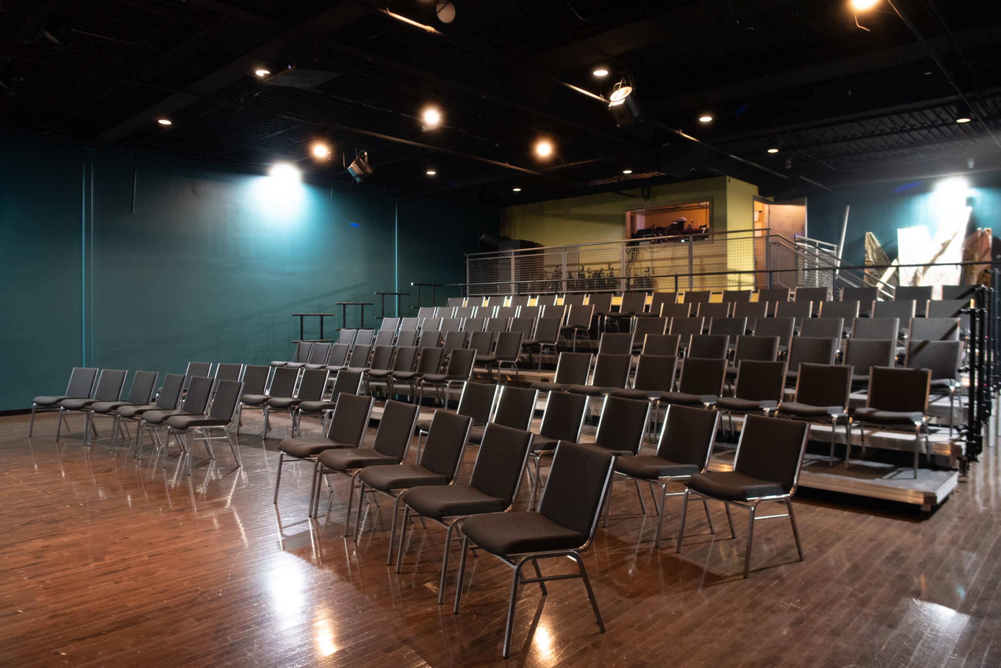 A row of empty folding chairs arranged in tiered seating in a dimly lit auditorium.