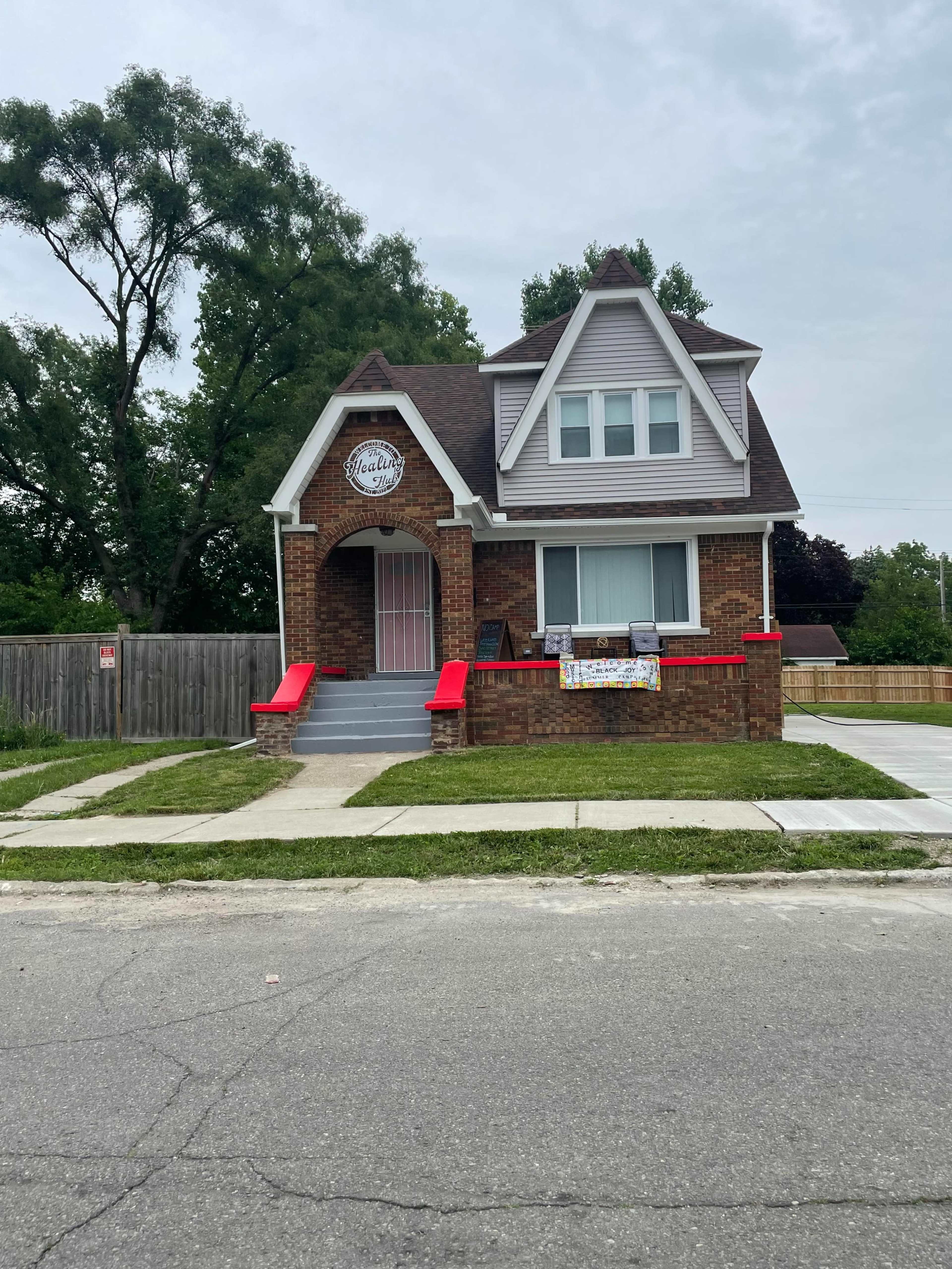A brick house with a gabled roof features red steps and a sign above the entrance.