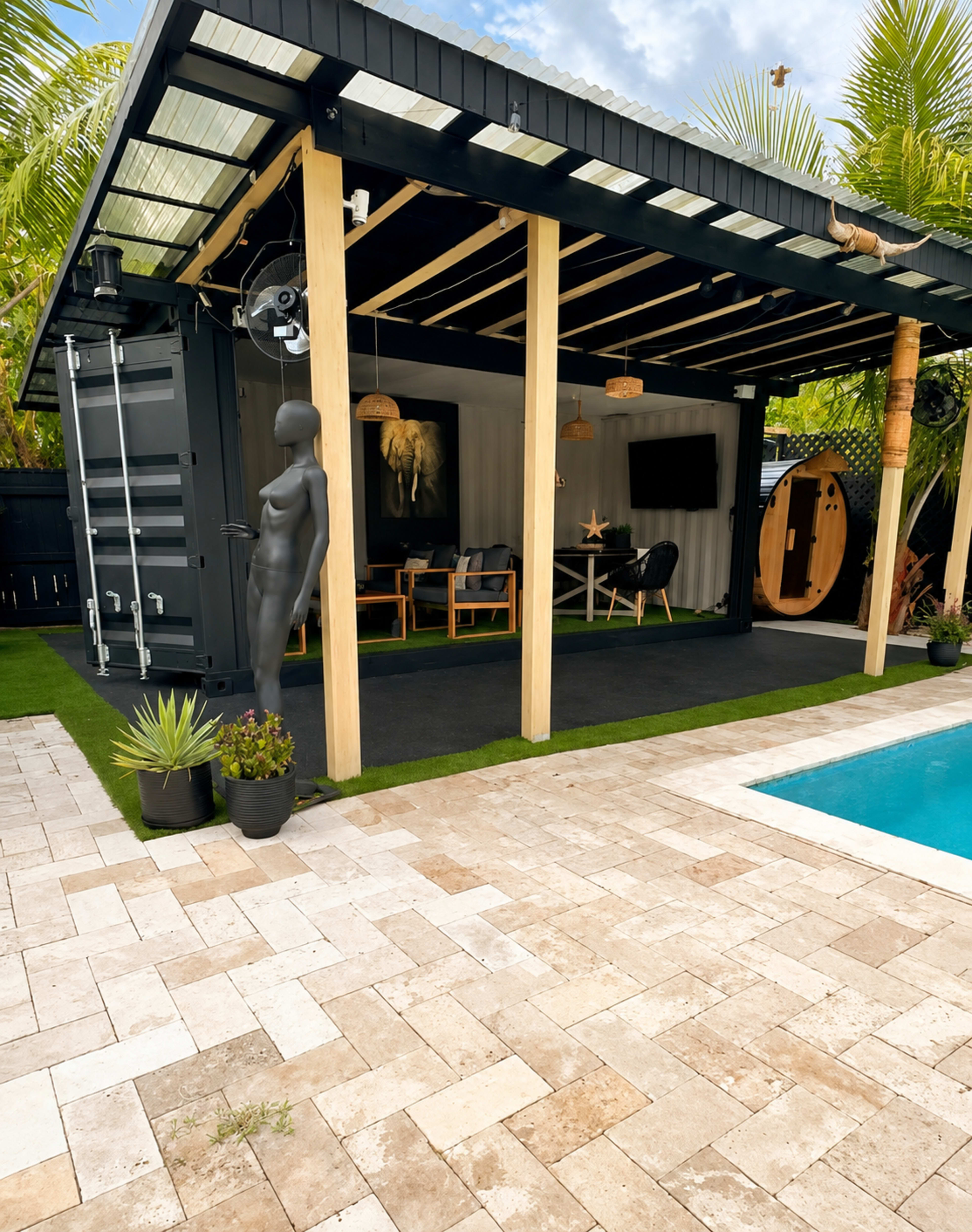 A modern outdoor space features a container-style structure with wooden pillars, surrounded by greenery, a pool, and a sculpture of a mannequin.
