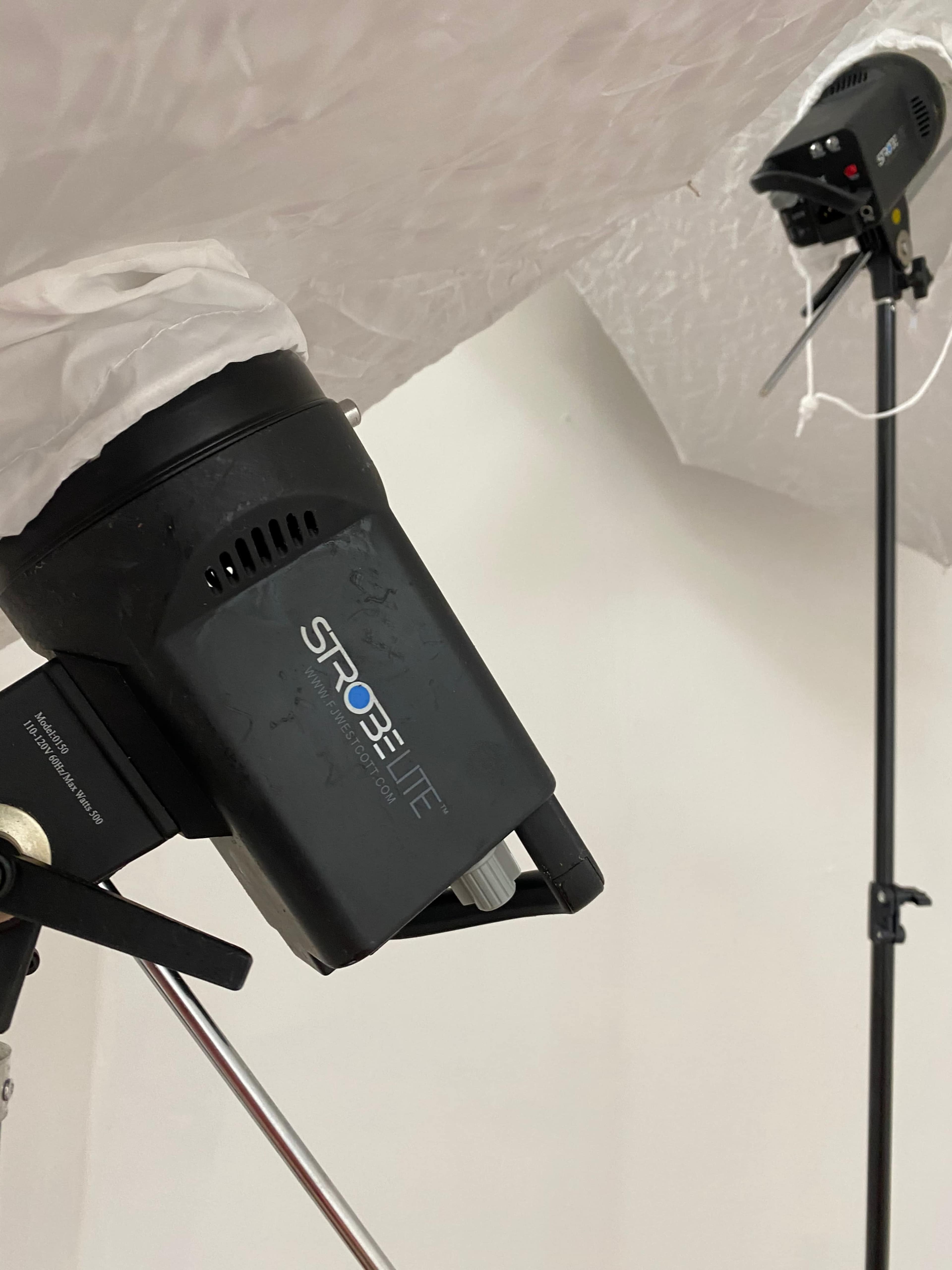 The image shows two strobe lighting equipment set up on stands against a white ceiling.
