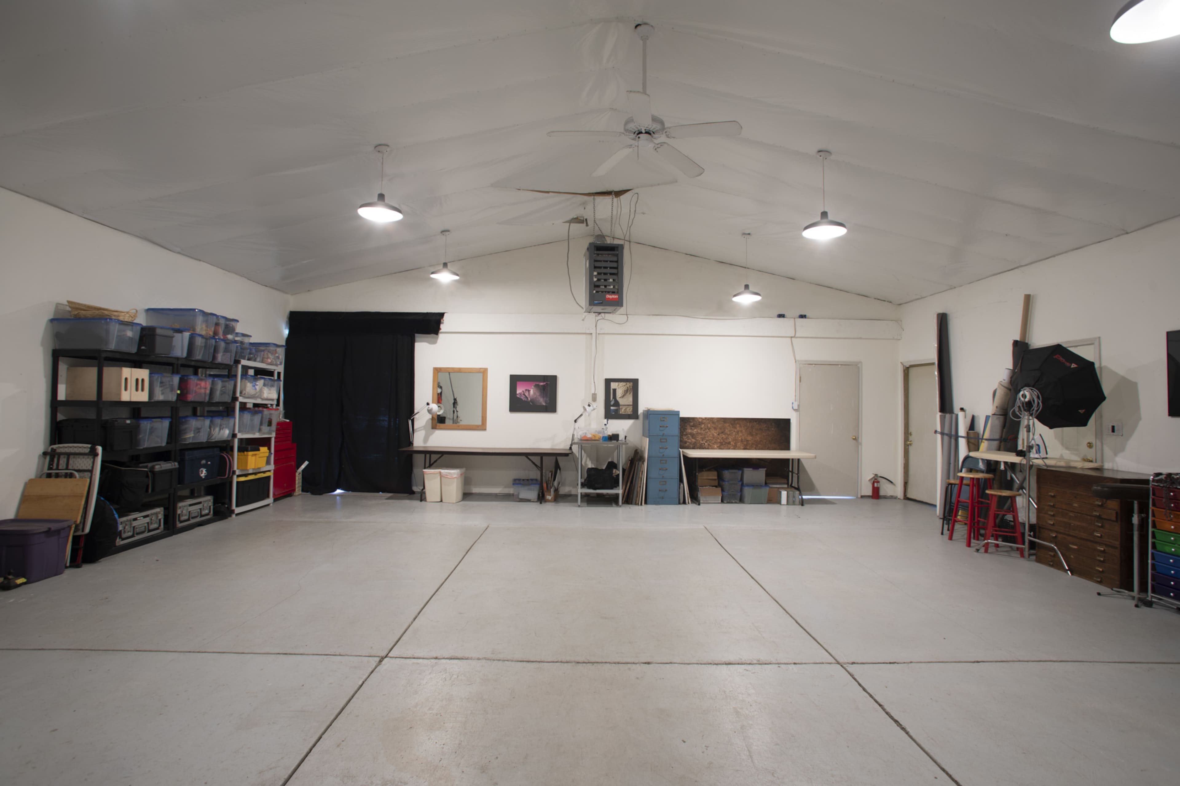 A spacious, well-lit room with a high ceiling, featuring various storage bins on shelves, a table in the center, and a few pieces of equipment along the walls.