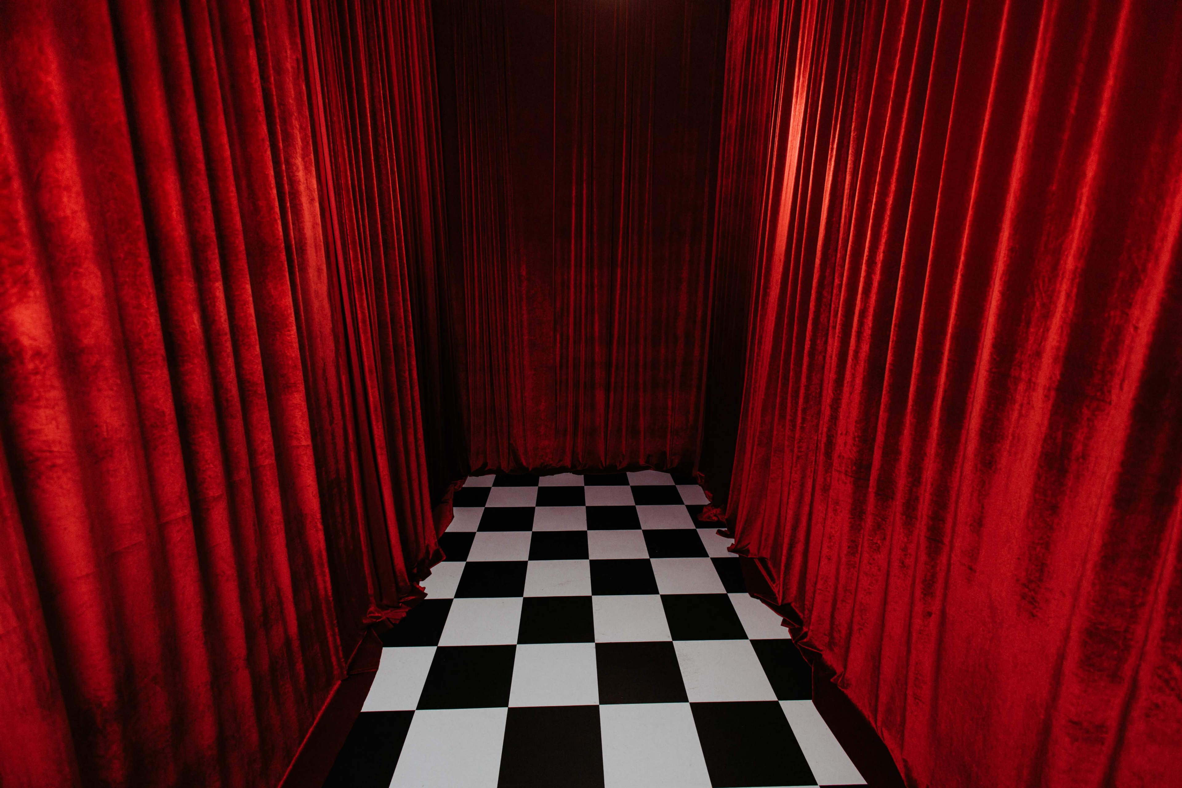 A narrow corridor features red velvet drapes on the walls and a black-and-white checkered floor.