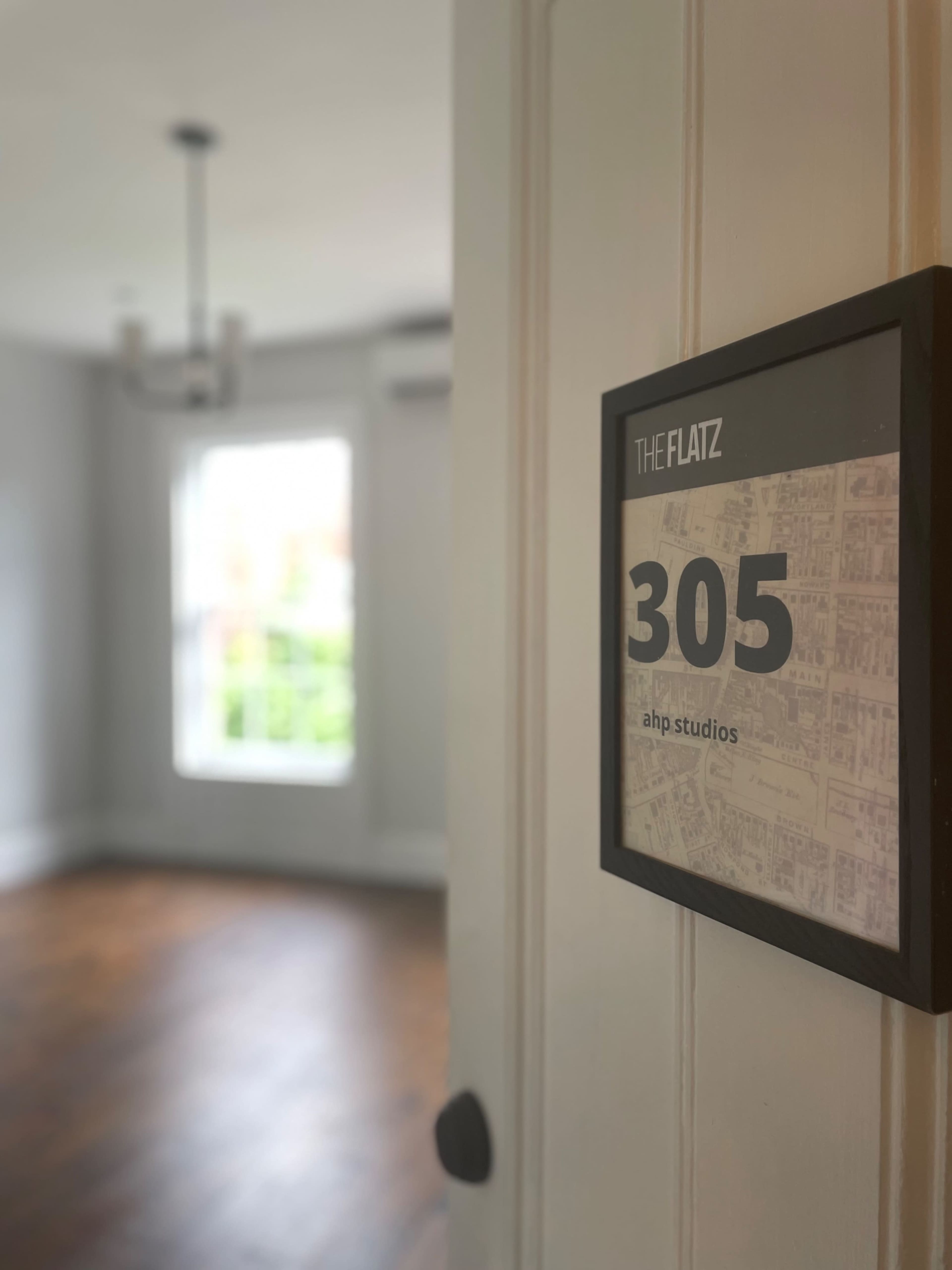 An open door revealing a room with a window, hardwood flooring, and a sign indicating "305 ahp studios."