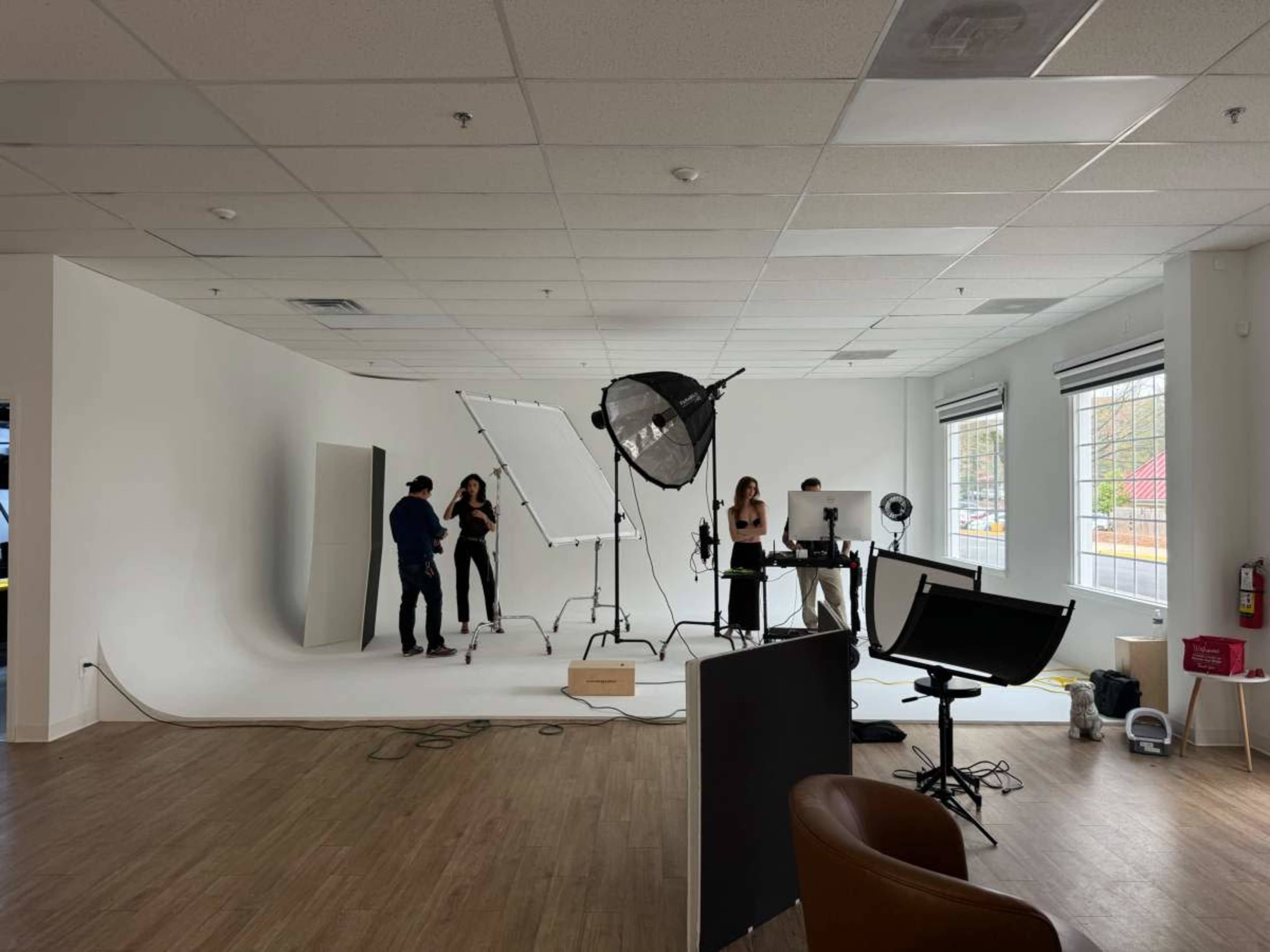 A photography studio setup features a large backdrop, lighting equipment, and four individuals preparing for a shoot.