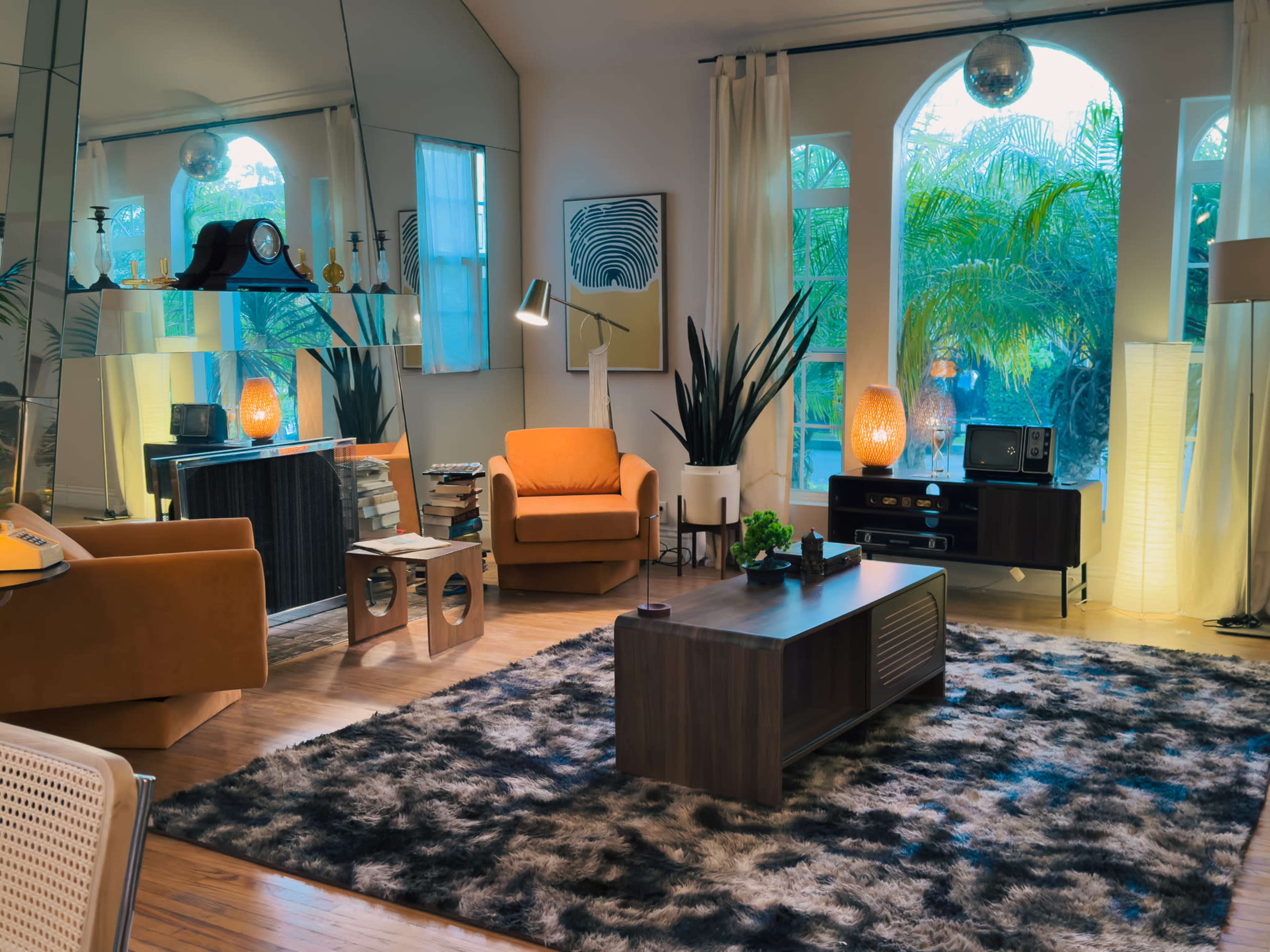 The image depicts a modern living room with a large area rug, an orange armchair, a coffee table, and large windows allowing natural light to enter.