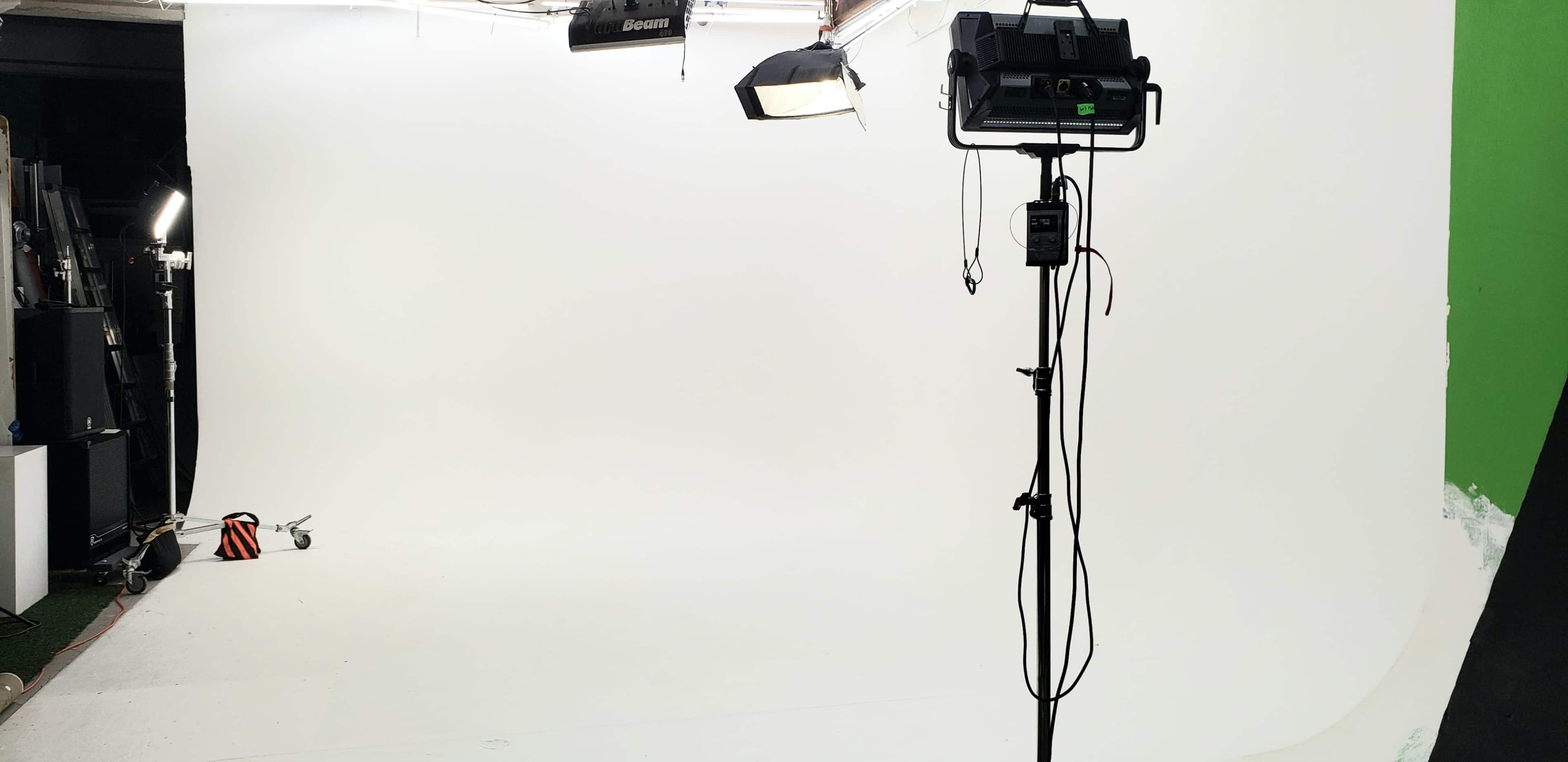 The image shows a photography studio with a seamless white backdrop, a lighting setup, and a tripod for equipment.