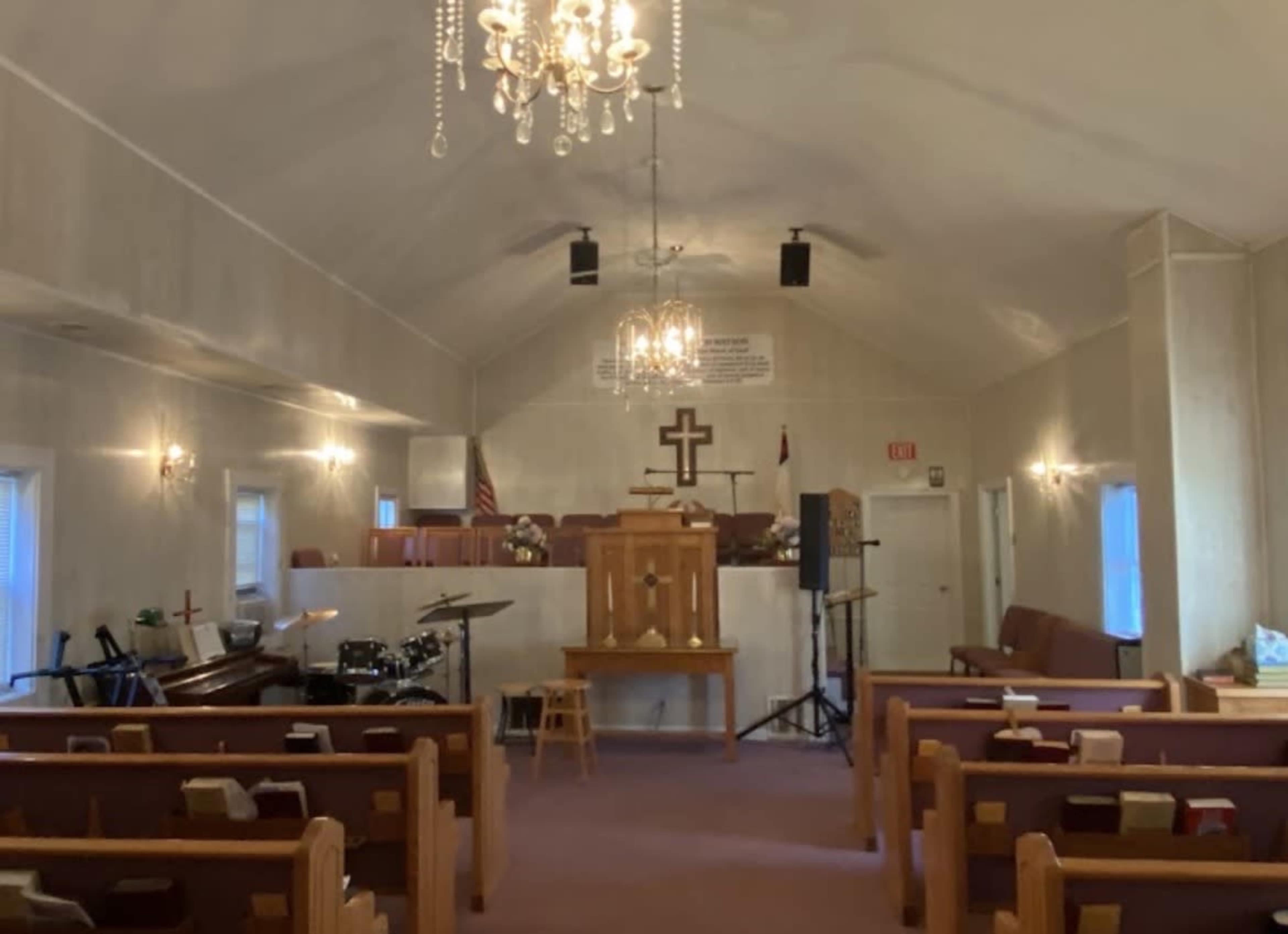 The interior of a church is shown, featuring pews, a pulpit, a drum set, and a chandelier hanging from the ceiling.