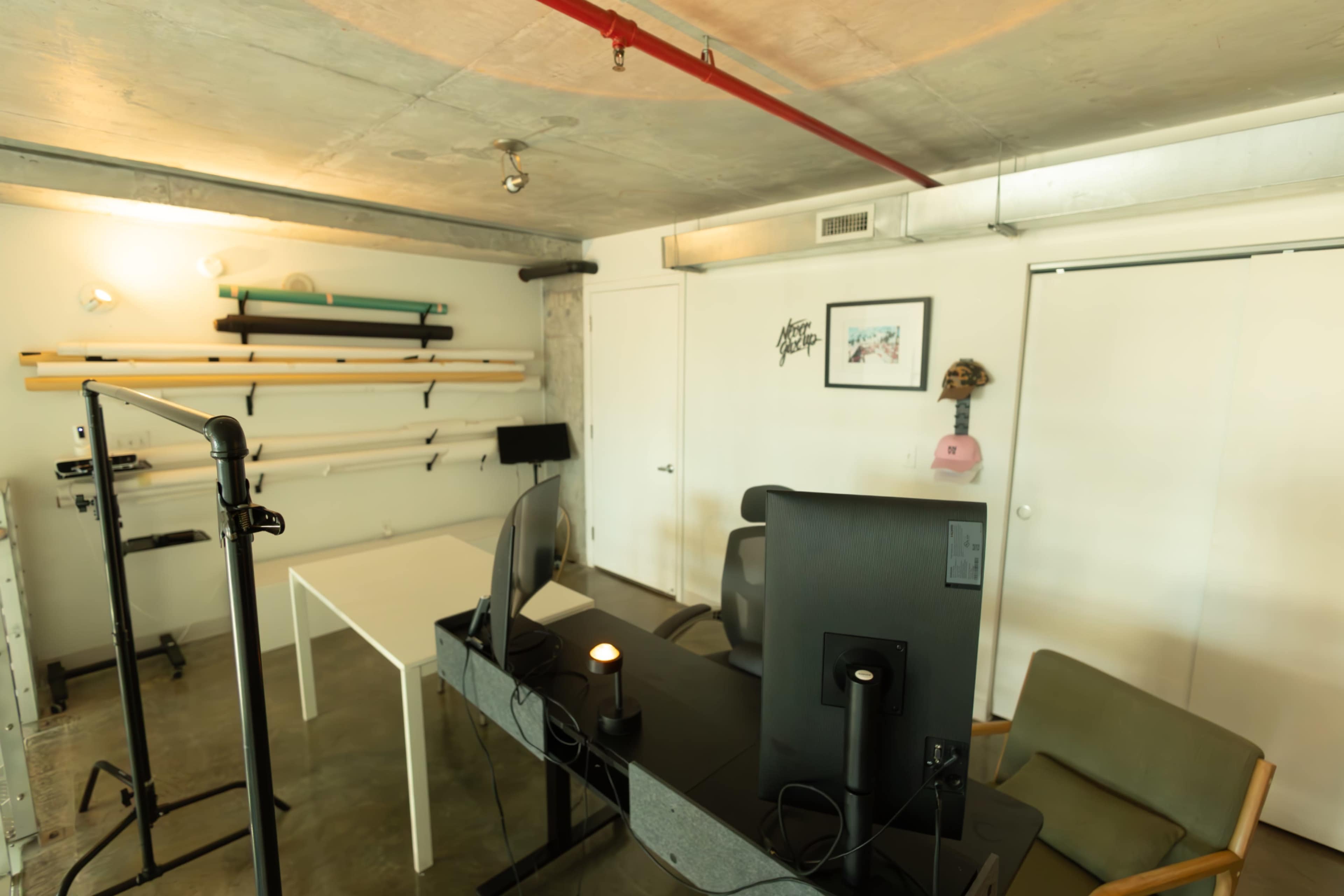 The image shows a modern office space with a desk, chairs, and shelving against a concrete wall.
