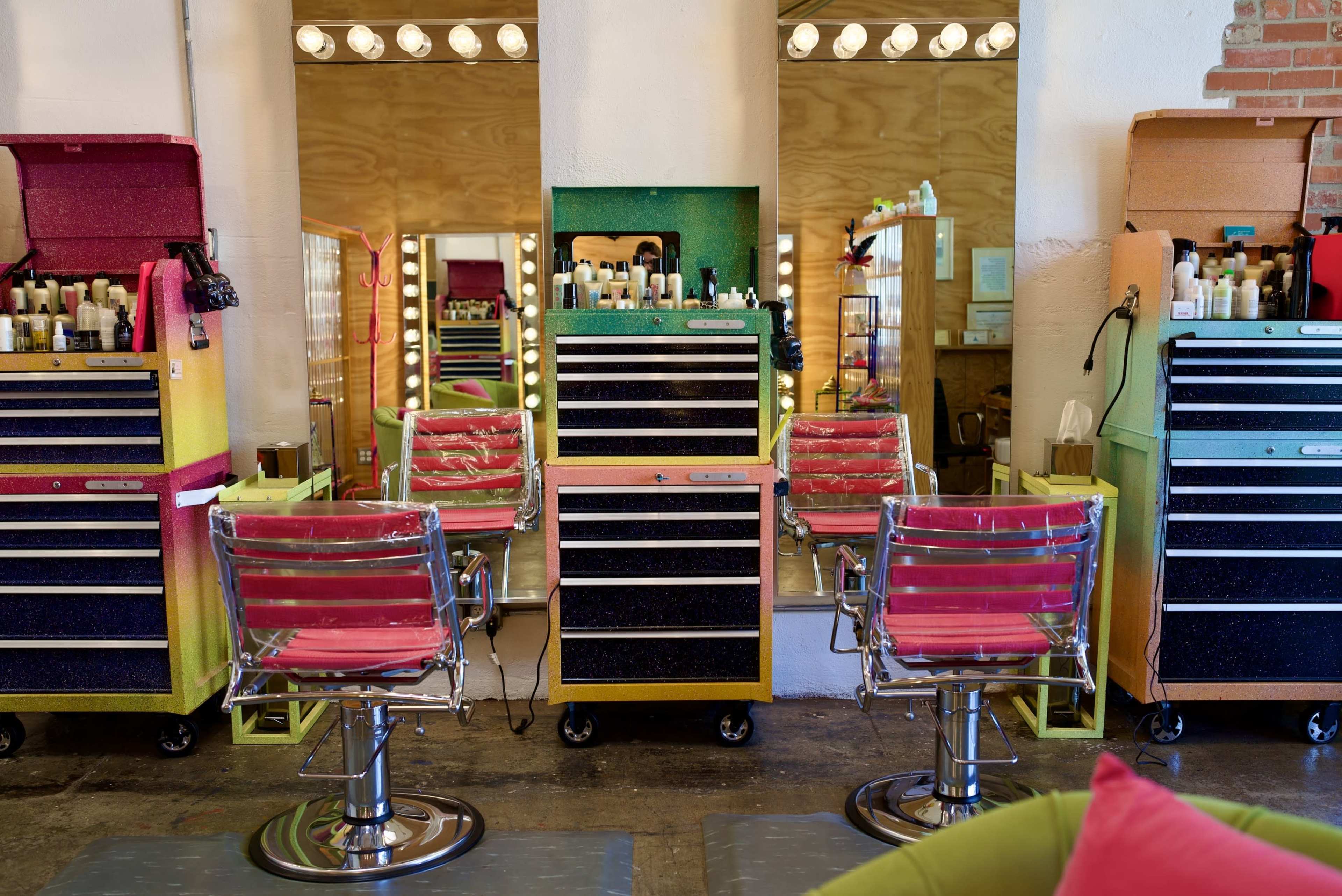 The image shows a brightly colored hair salon interior with multiple styling stations equipped with mirrors and salon tools.