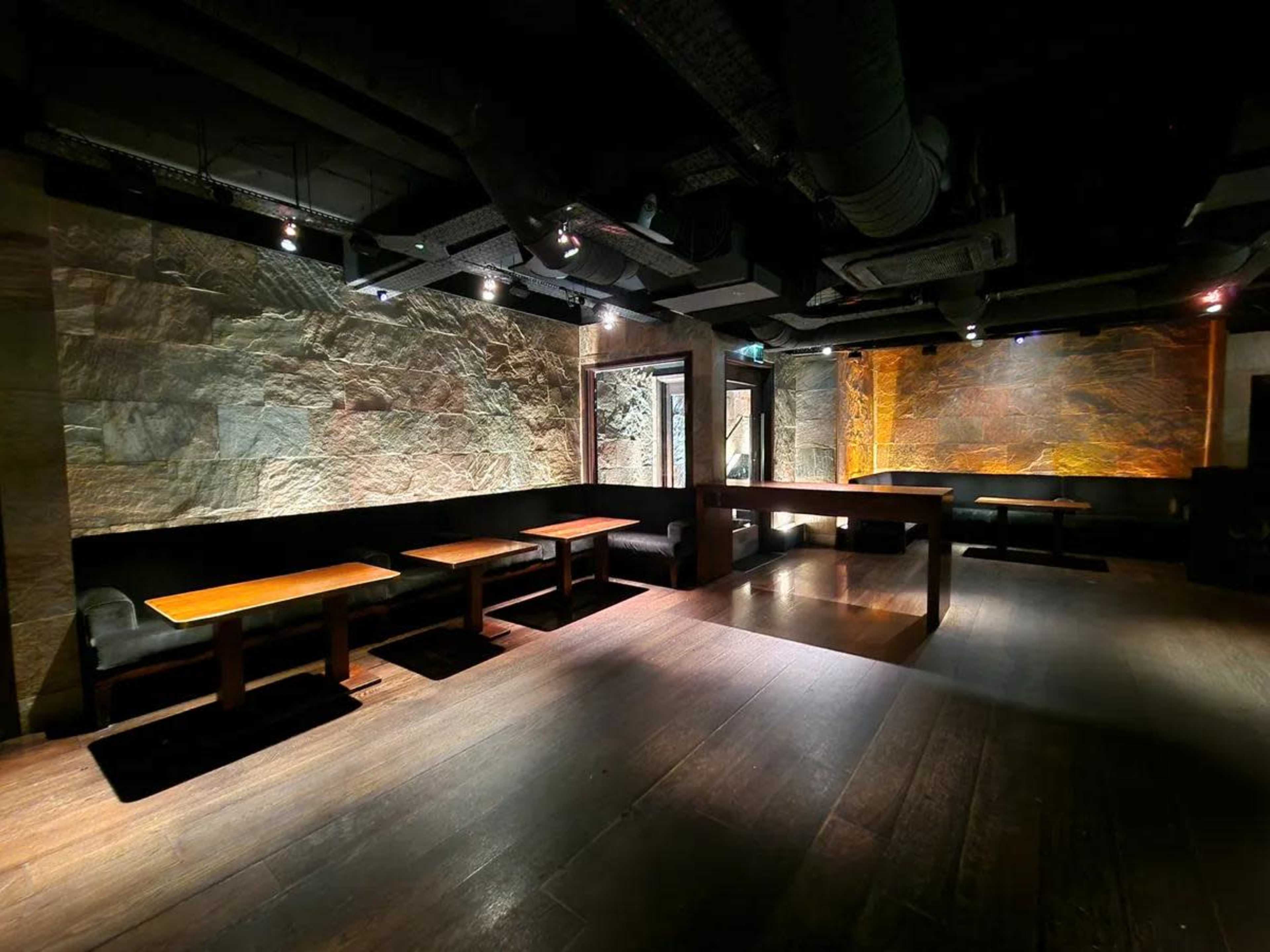 The image shows a dimly lit interior of a restaurant or bar with wooden tables and stone-textured walls.