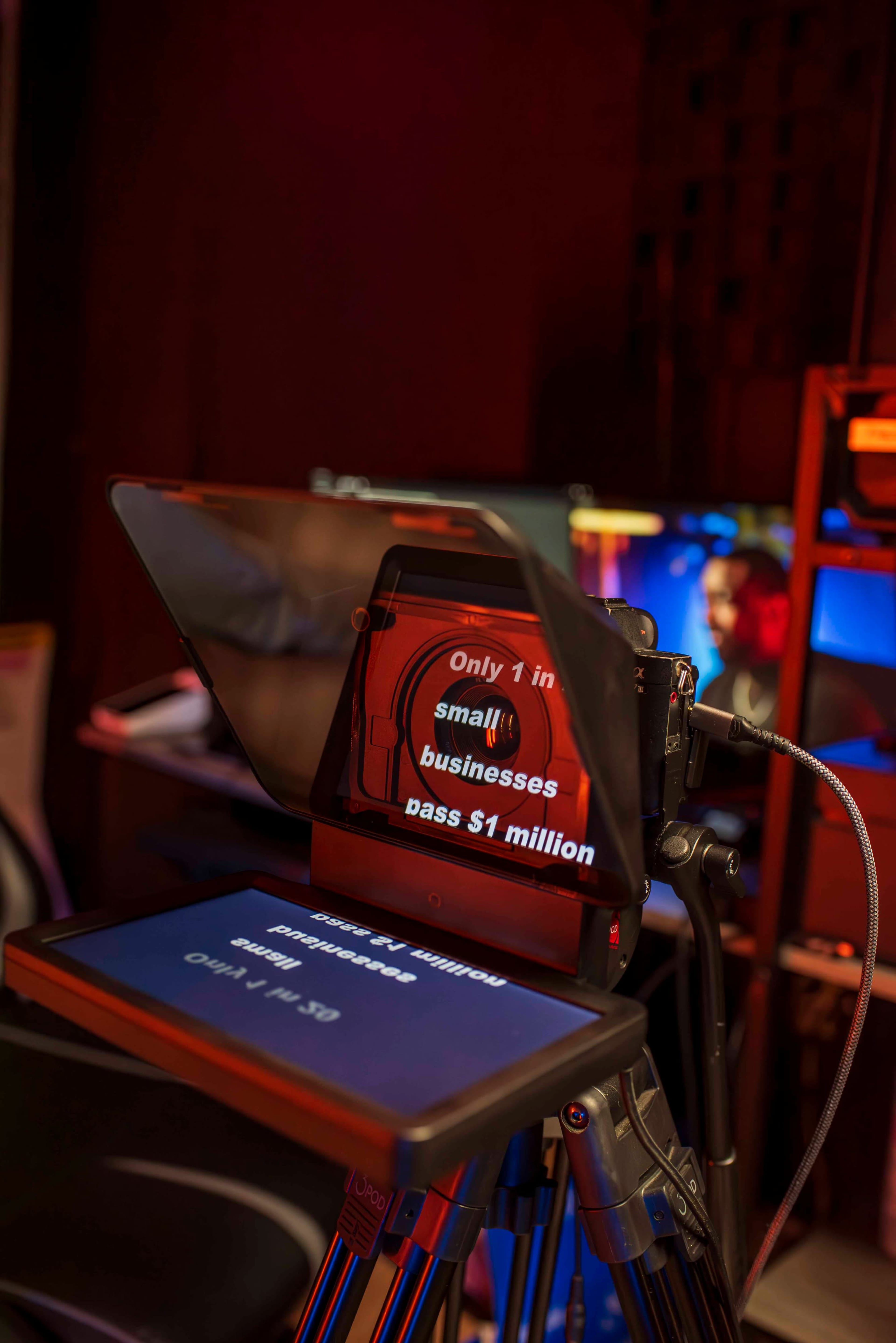 A teleprompter displays the message "Only 1 in small businesses pass $1 million" in a dimly lit room.