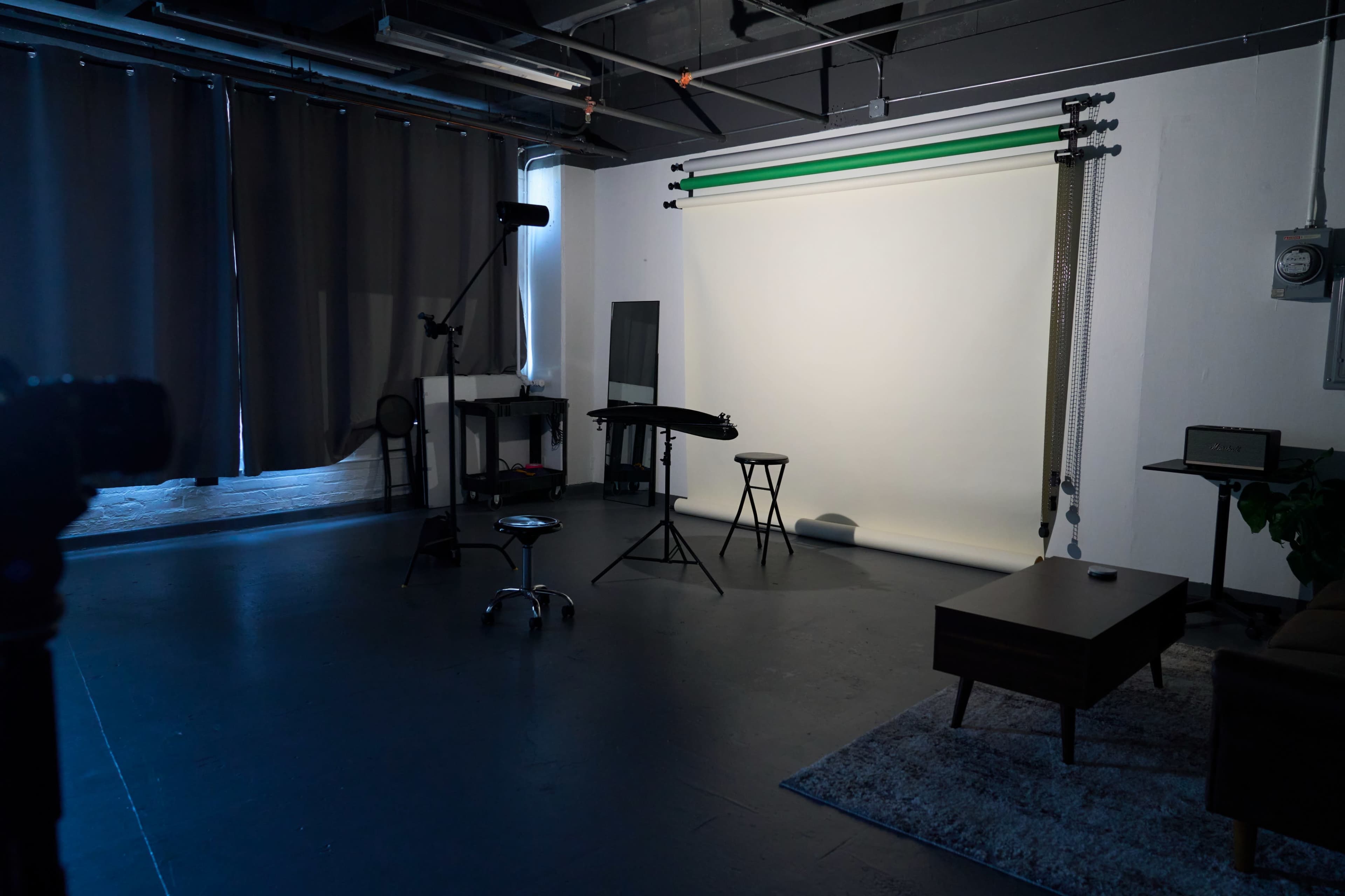 A photography studio with a backdrop, a stool, and various equipment in a dimly lit space.