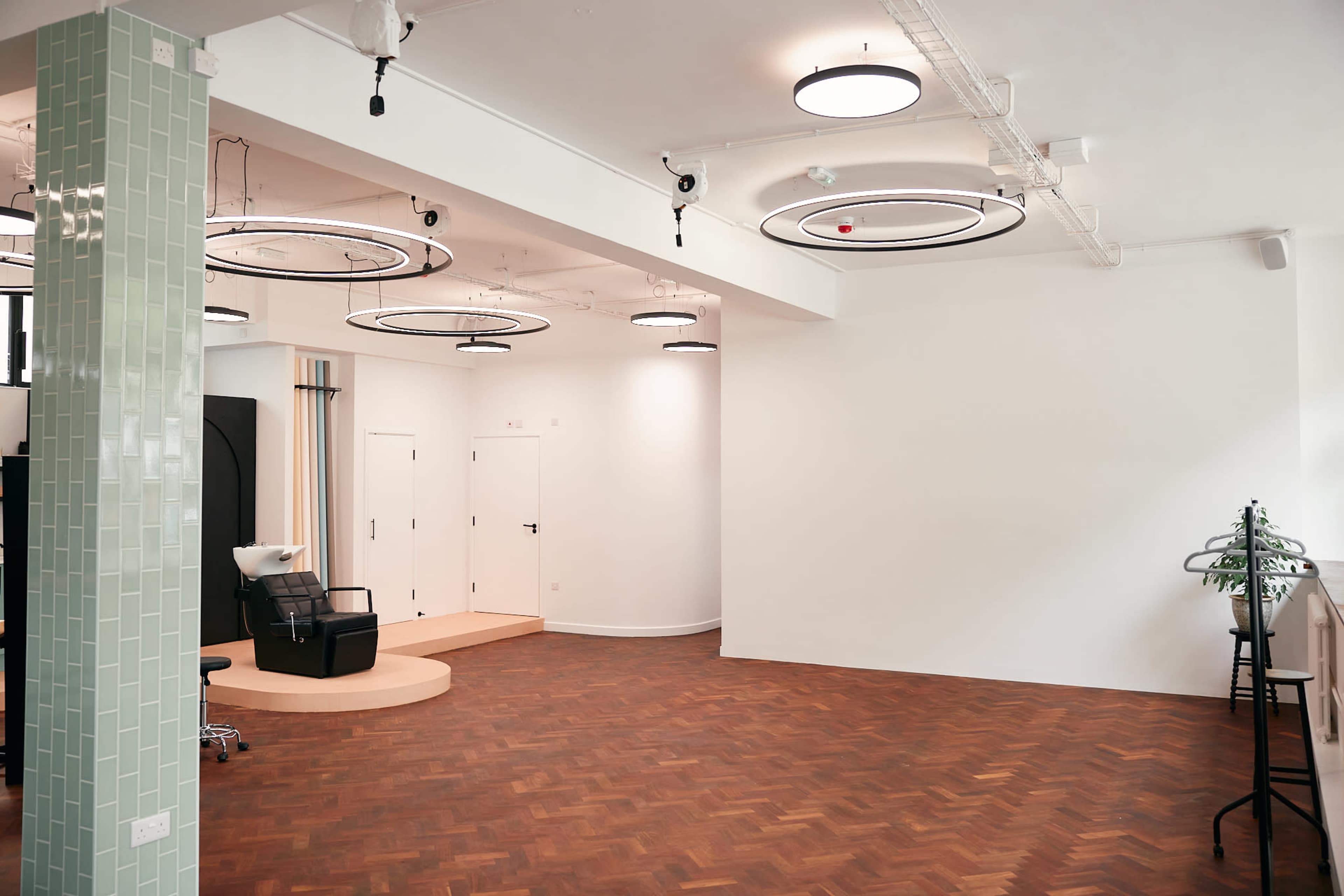 A modern, well-lit salon space featuring a black salon chair, a shampoo station, and circular ceiling lights in a room with hardwood flooring.