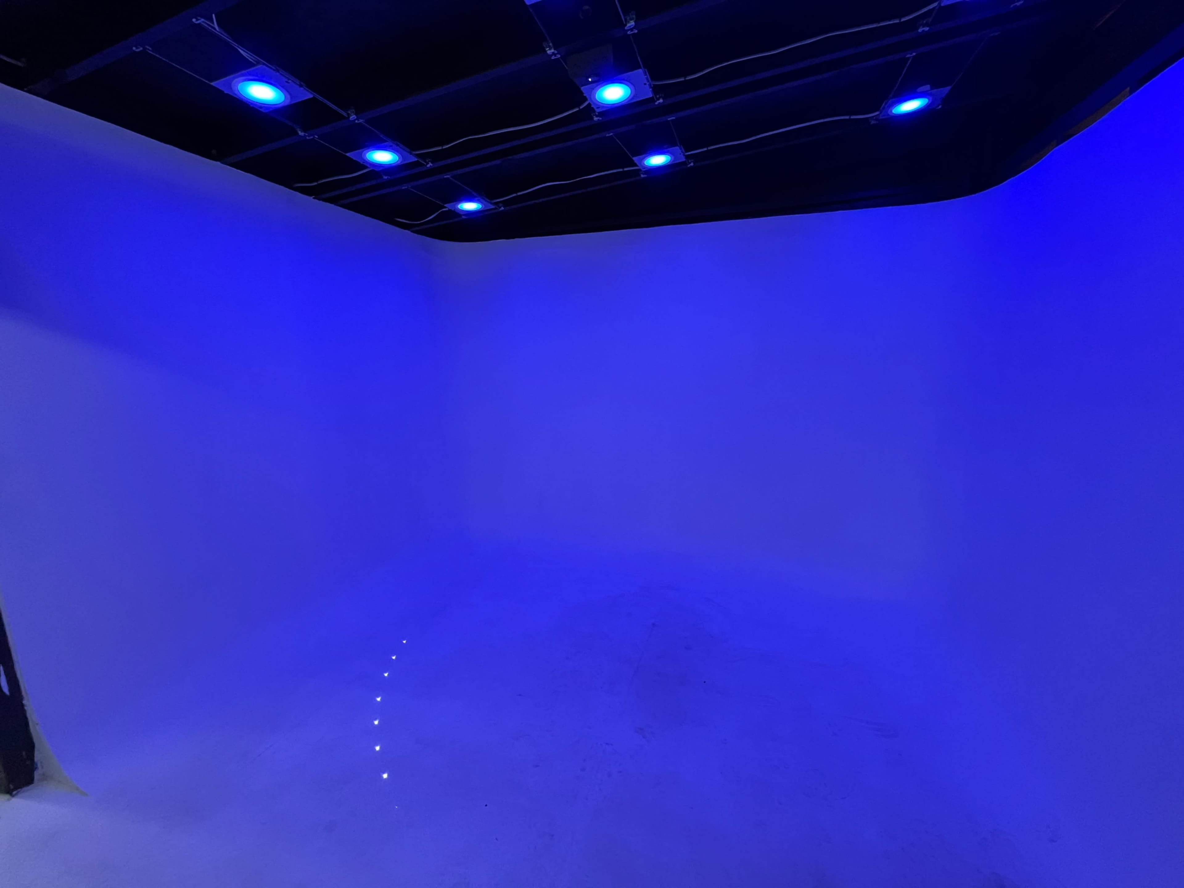 The image shows a minimalist room with blue lighting and a smooth white backdrop.